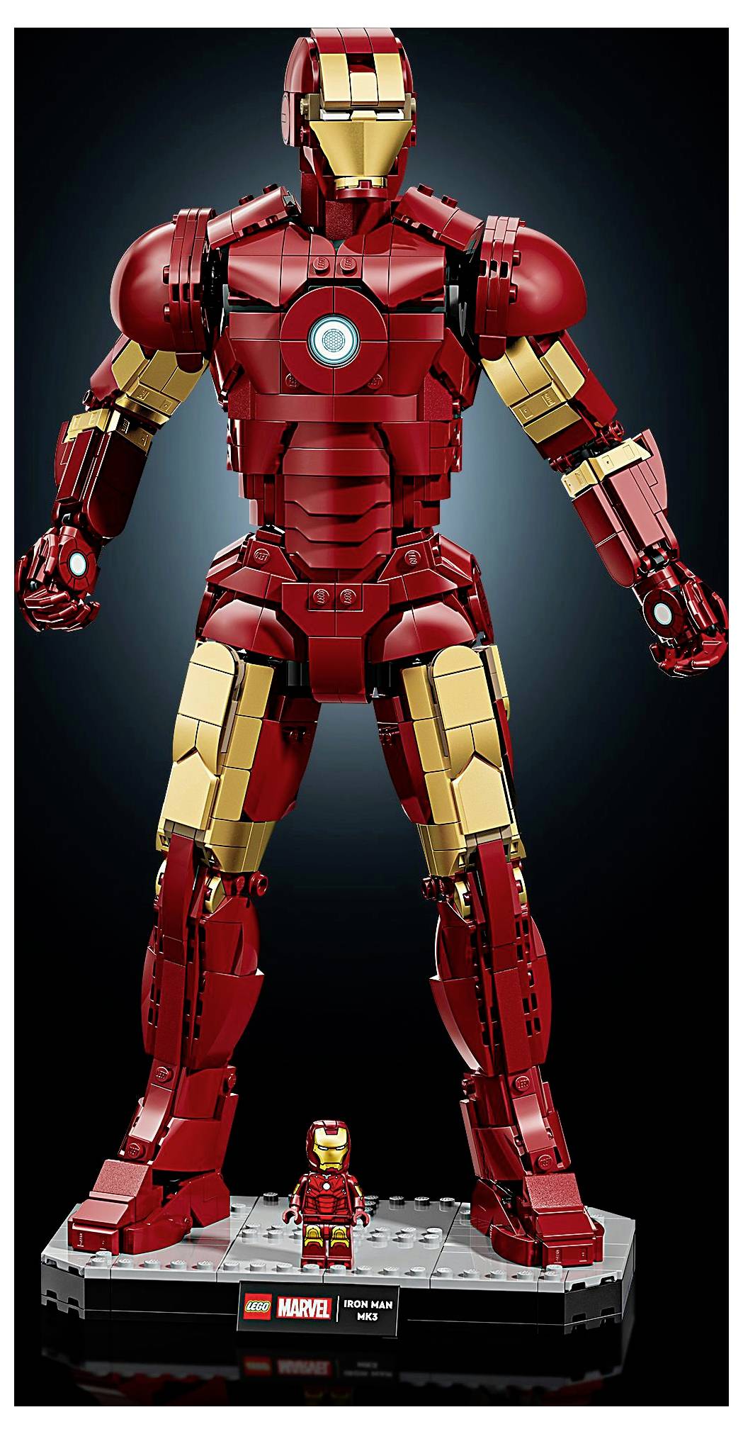 Lego model červeného a zlatého obrněného superhrdiny stojícího na výstavním podstavci, s menší odpovídající Lego figurkou před ním.