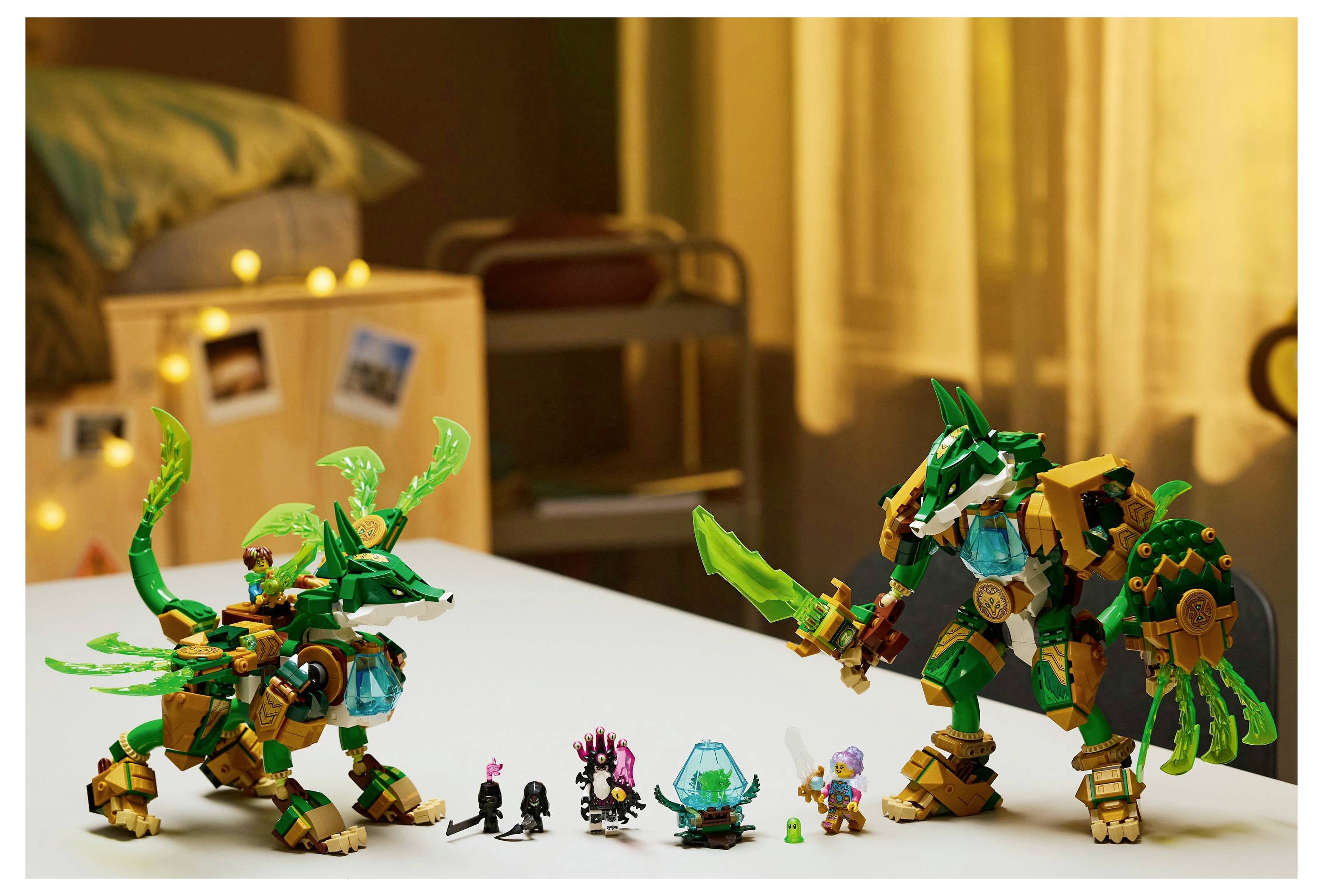 Dva hračkářské figurky připomínající draka a robotického válečníka jsou vystaveny na stole, obklopeny menšími hračkami a doplňky.