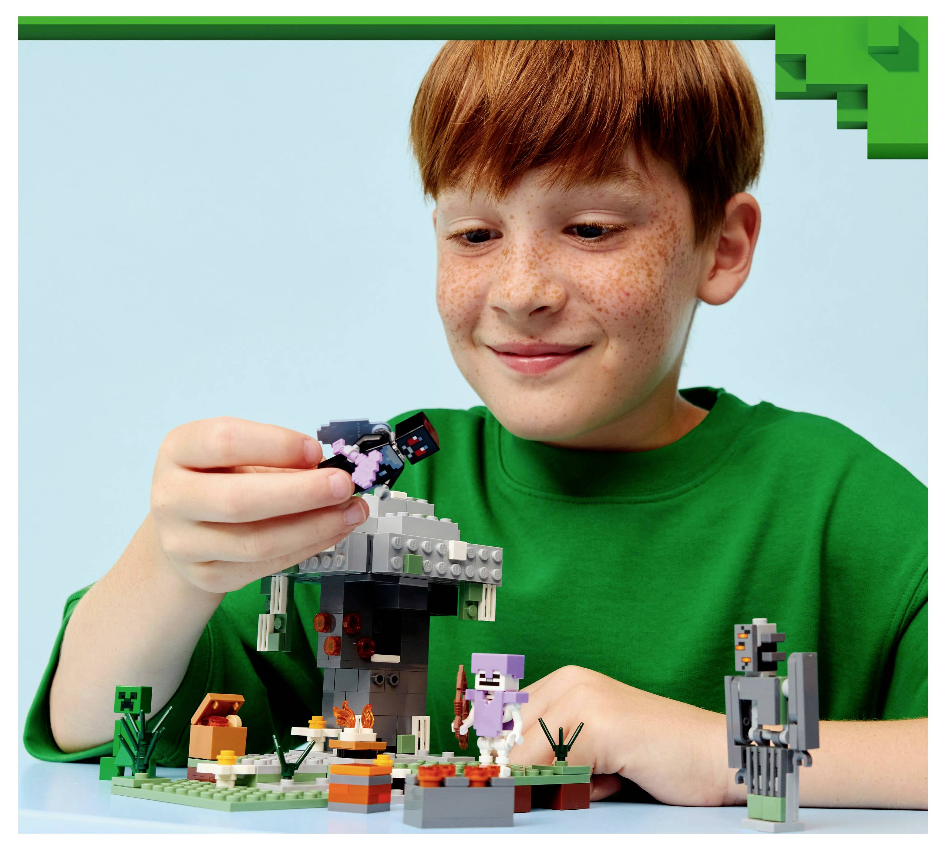 Dítě v zelené košili si hraje se sadou LEGO, která zobrazuje scénu z Minecraftu s malými postavičkami a doplňky na stole.