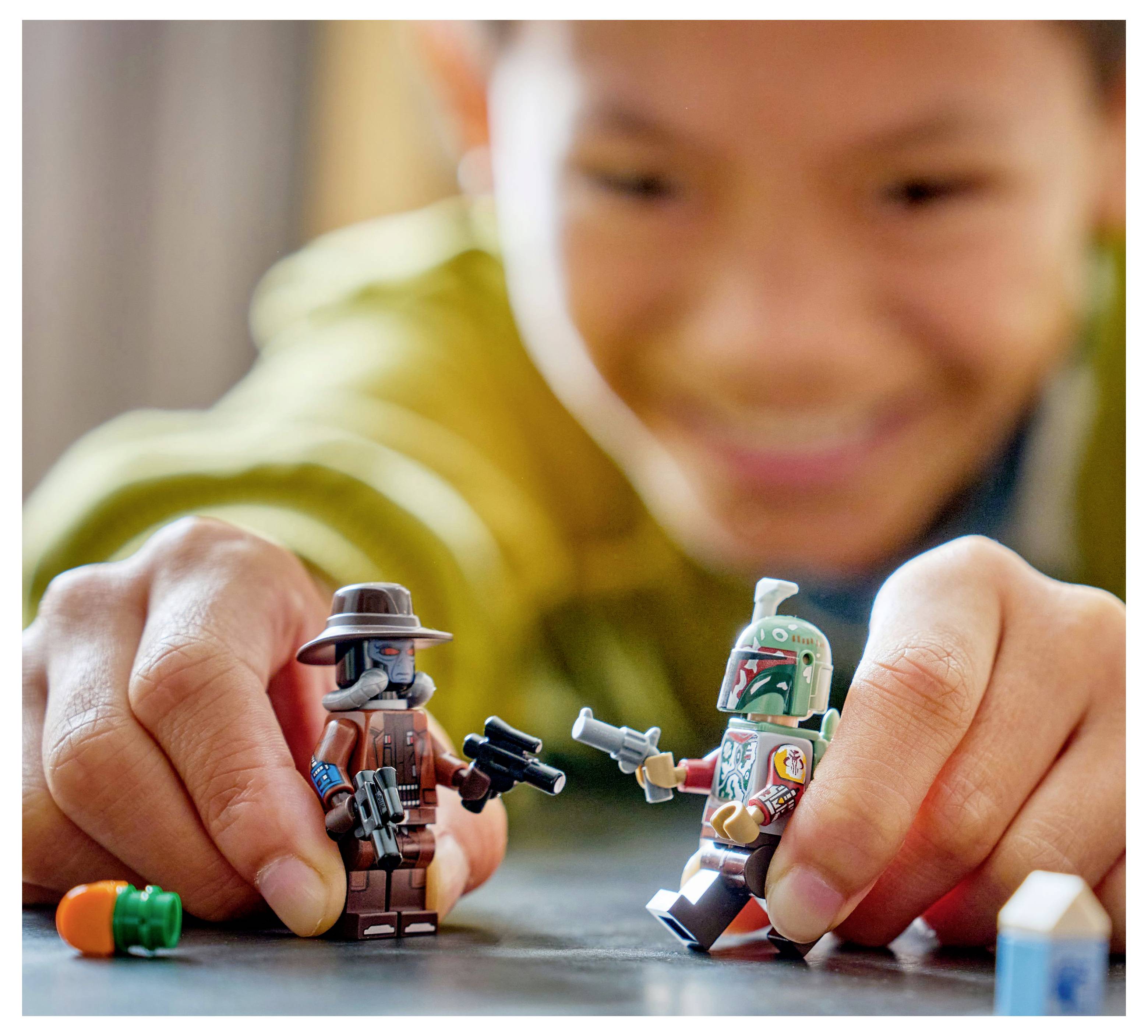 Dítě si hraje s dvěma LEGO figurkami na stole, usmívá se a zapojuje se do imaginativní hry.
