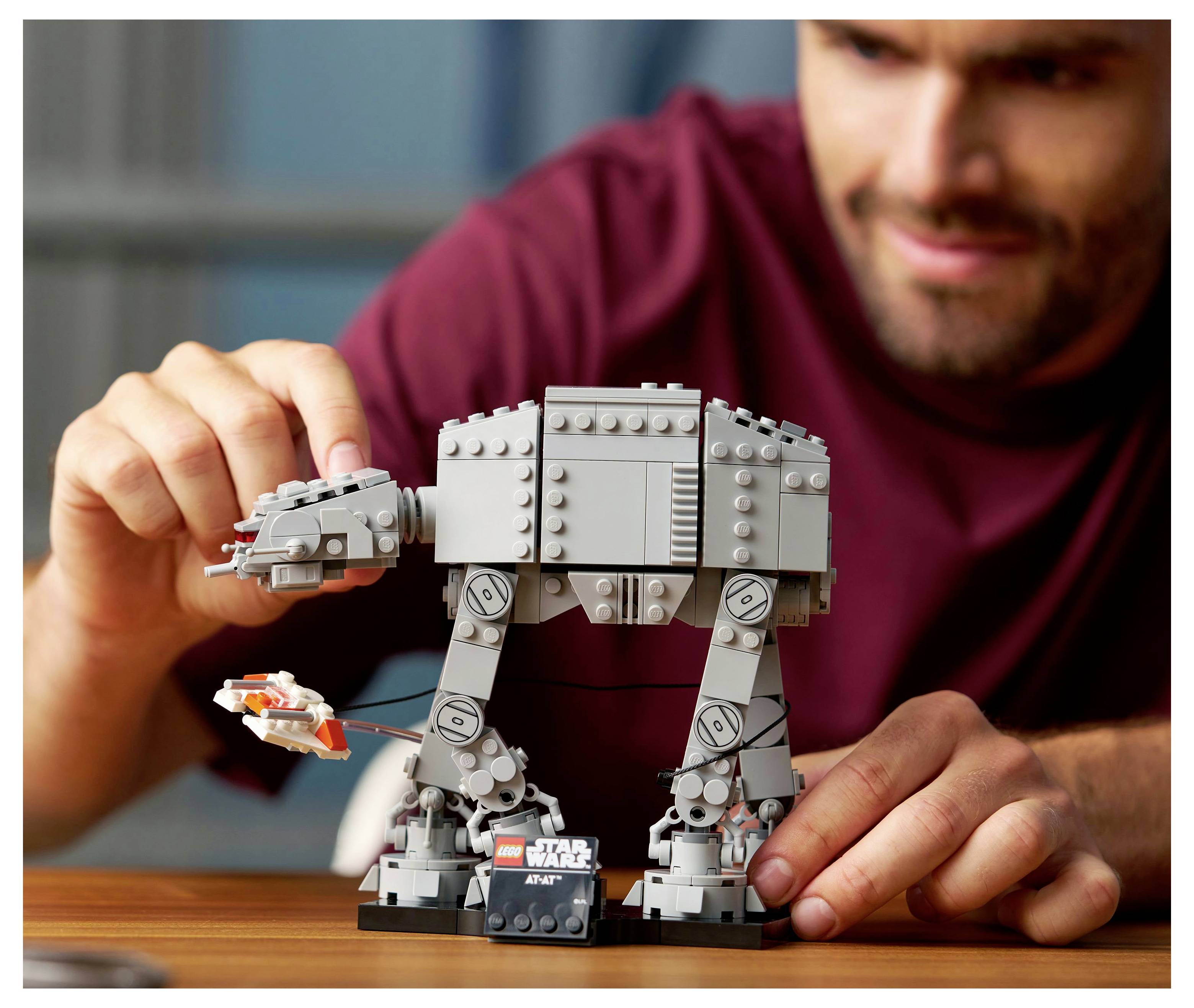 Osoba sestavuje model LEGO 'Star Wars AT-AT' s kloubovýma nohama a malou hvězdnou lodí, což naznačuje aktivitu zaměřenou na budování scény.