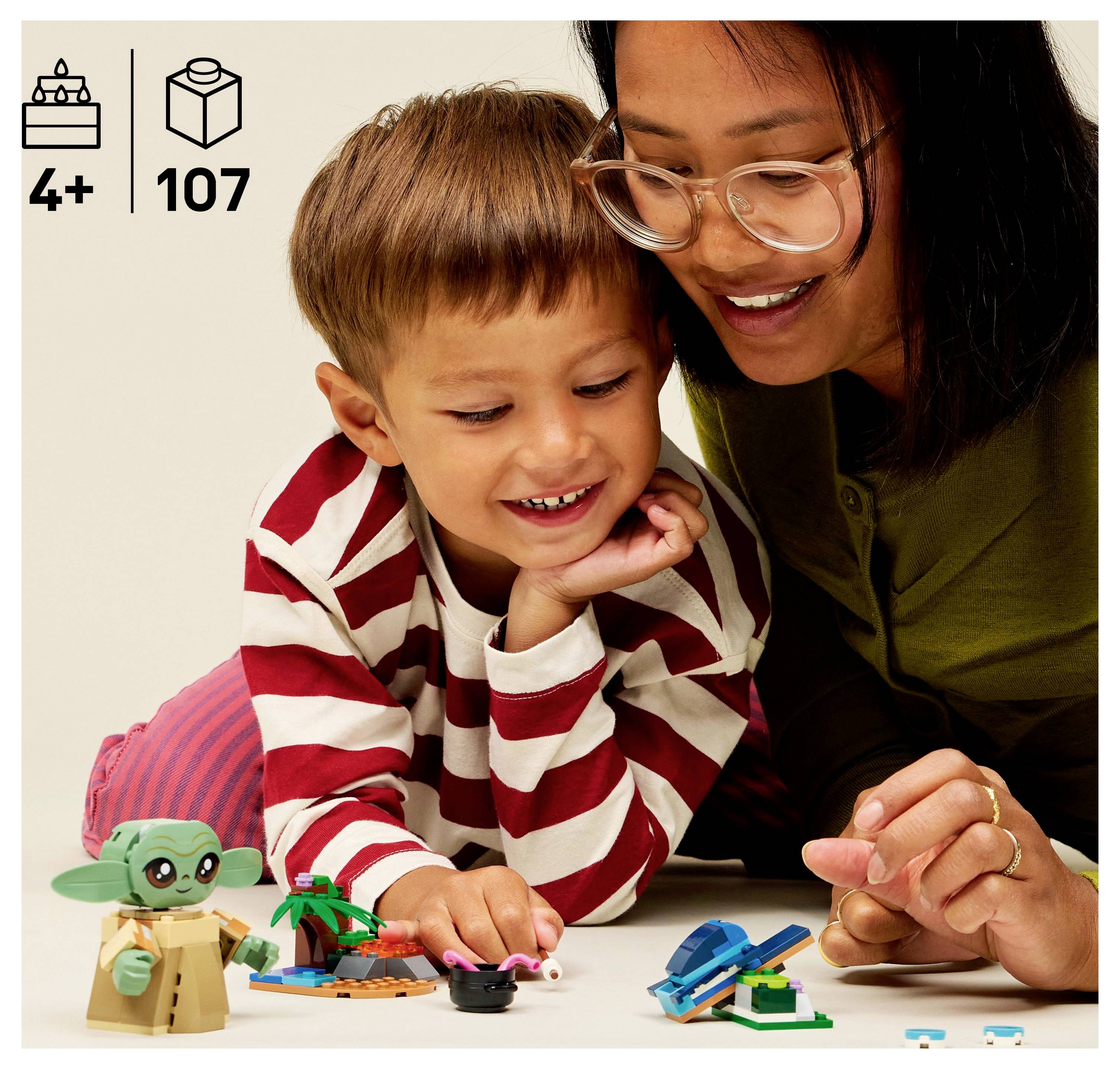 Žena a dítě si hrají s malými hračkami na bílém povrchu. Dítě má na sobě pruhované tričko a žena nosí brýle.