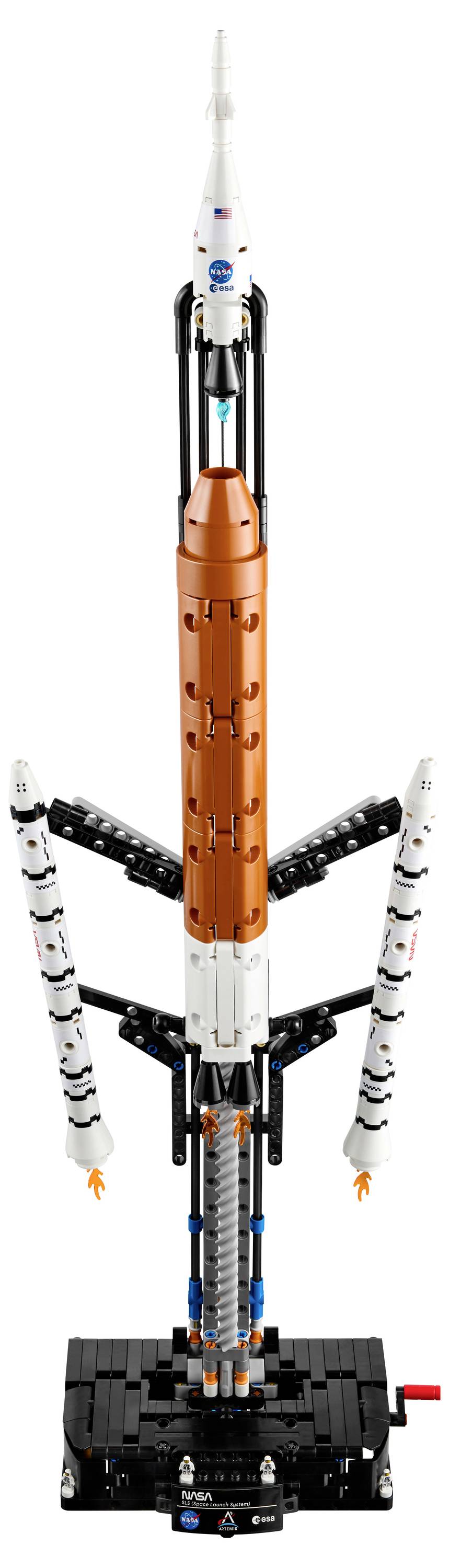 Model rakety s oranžovými a bílými díly, po stranách opatřený menšími pomocnými raketami, umístěný na černém podstavci.