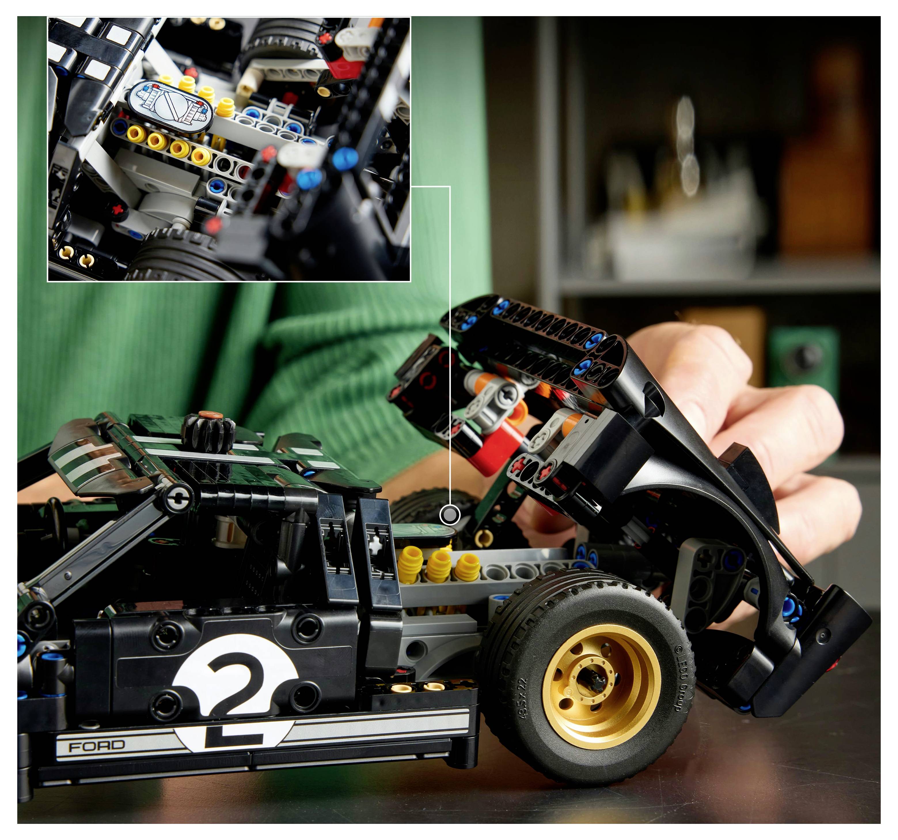 Osoba sestavuje detailní modelovou hračku automobilu se zřetelným motorem a koly. Vložený obrázek ukazuje detail mechaniky vozu.
