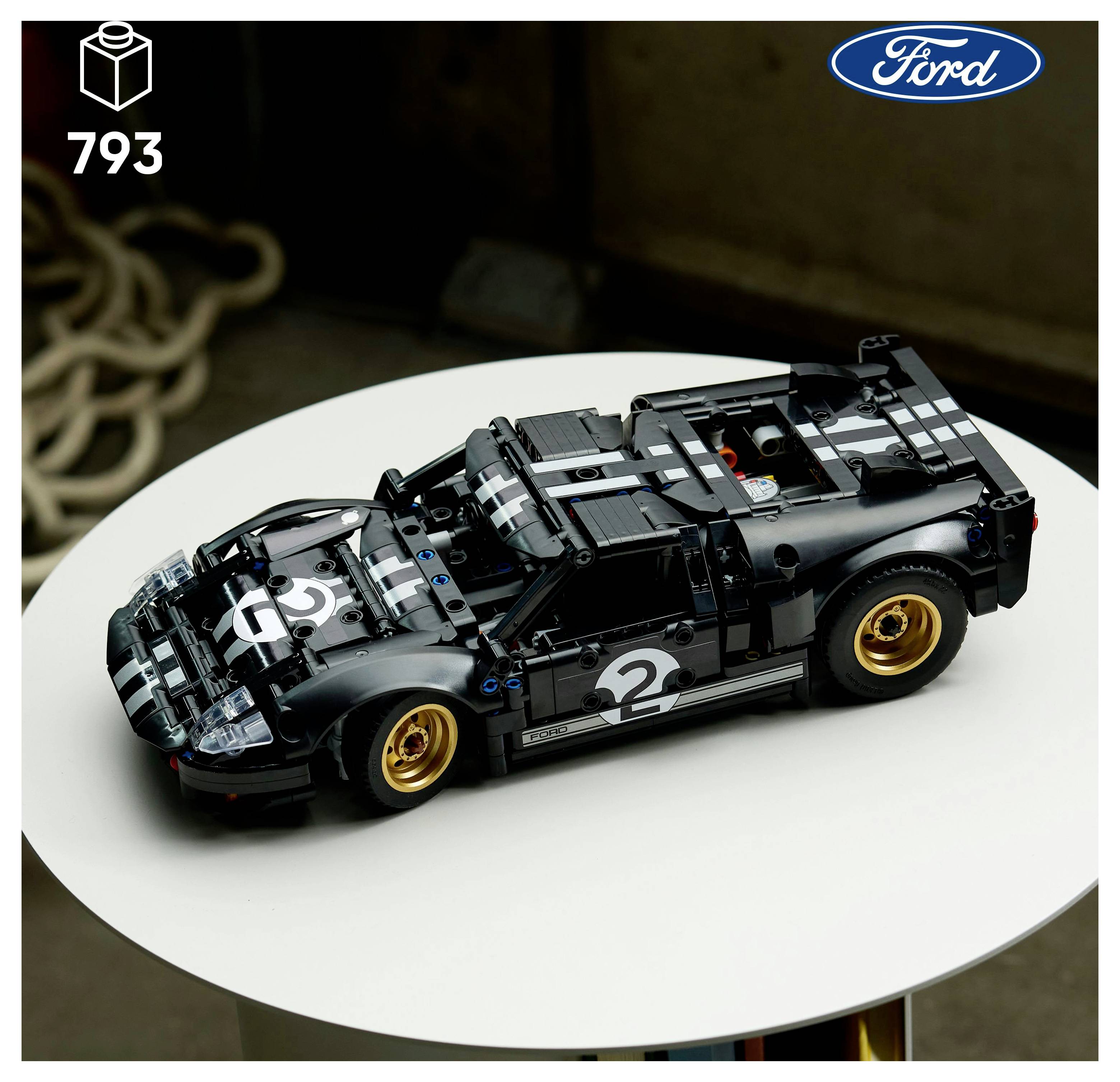 Černý model Ford GT z kostek LEGO s Racing pruhy a zlatými ráfky umístěný na kulatém bílém stole. Logo Ford je v pravém horním rohu.