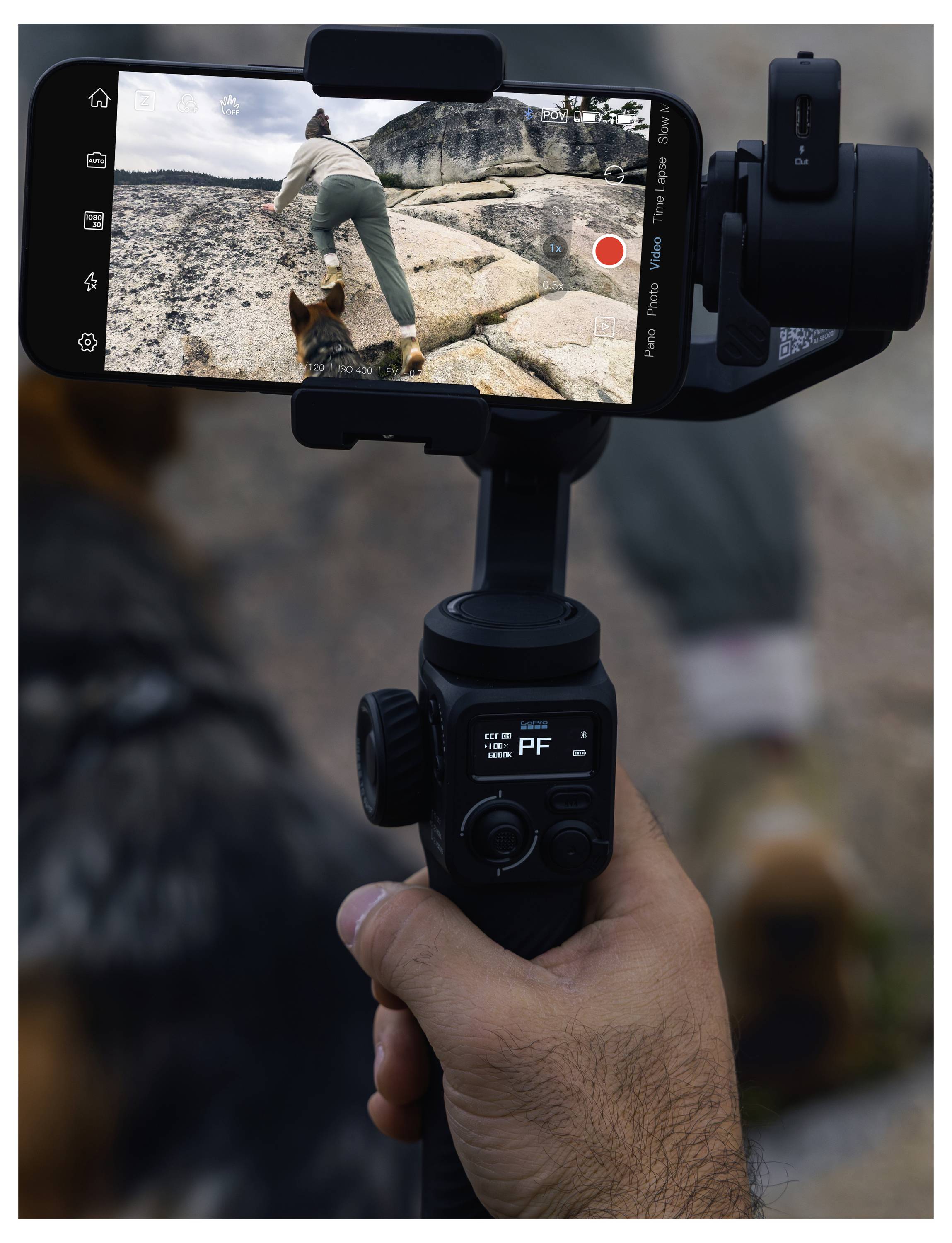 Osoba používá gimbal pro natáčení videa na smartphonu, přičemž zachycuje jinou osobu lezoucí po skalnatém povrchu. Na nahrávací obrazovce je zobrazen červený tlačítko záznamu.