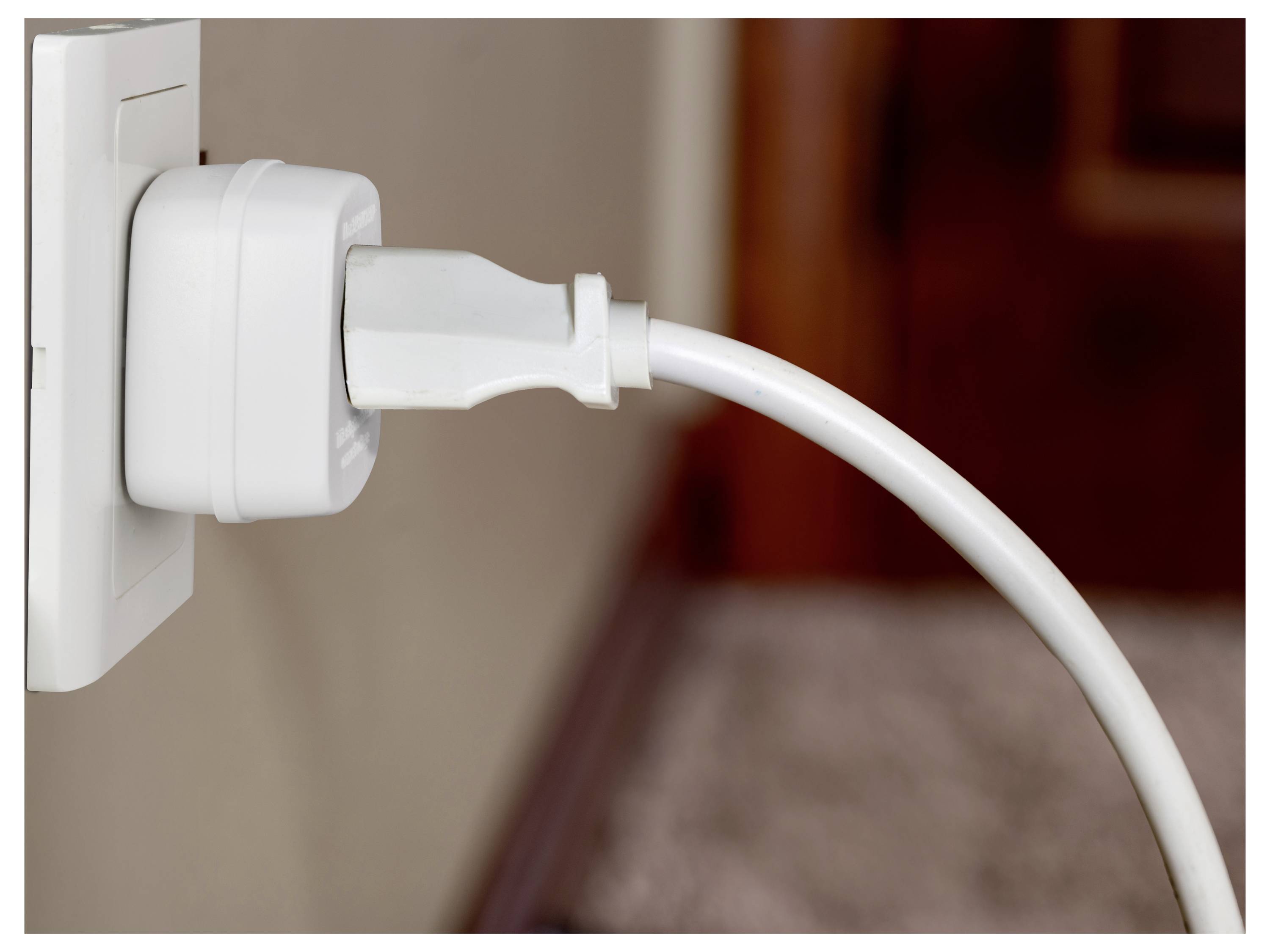 Bílá zástrčka je bezpečně připojena k elektrické zásuvce na stěně, s napájecím kabelem vedoucím z ní, což naznačuje aktivní používání.