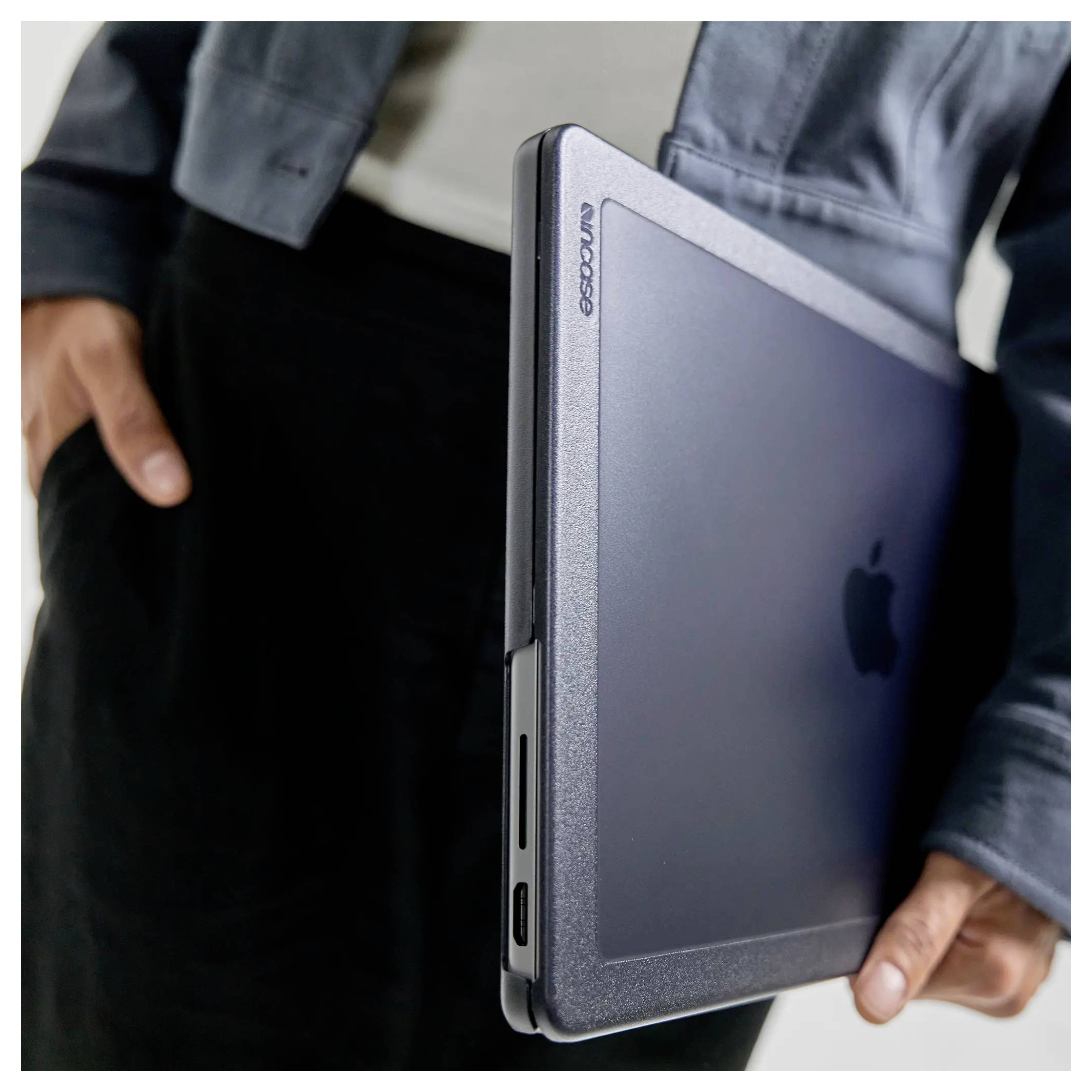 Osoba v bundě držící zavřený notebook s obalem 'Incase', na němž je vidět logo Apple, pohled z boku.