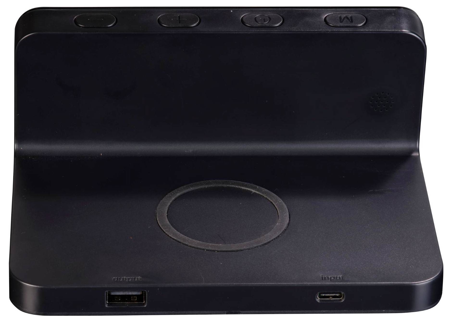Černá nabíjecí stanice s kruhovým nabíjecím podložkou na horní straně. Na přední straně se nachází USB port a USB-C port označený jako „In" a „Out".