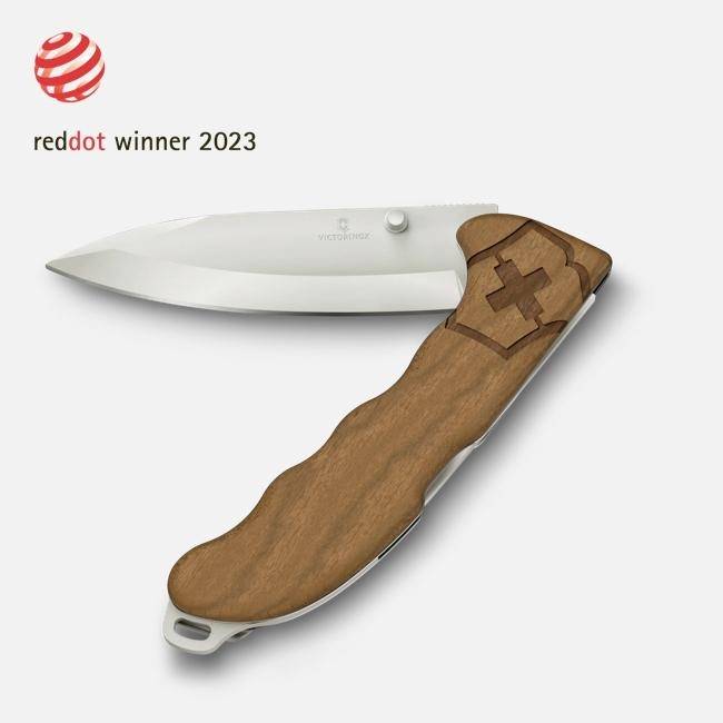 Victorinoxský skládací nůž s dřevěnou rukojetí a otevřeným nerezovým listem, v rohu označený „reddot winner 2023".