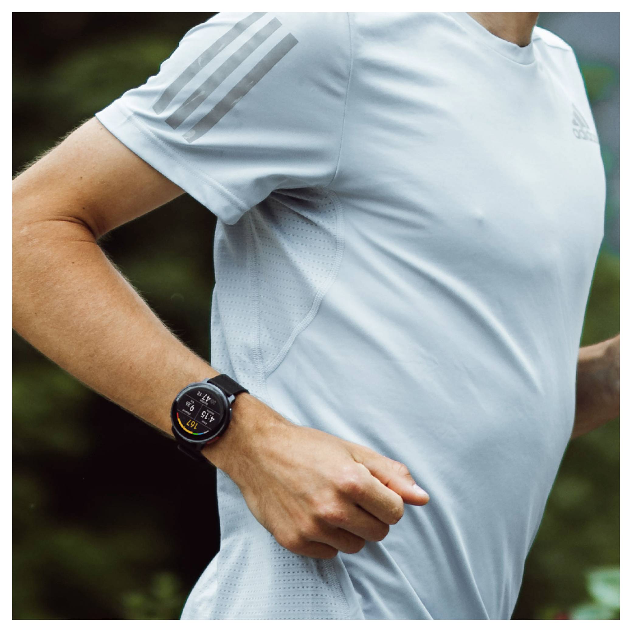 Běžec v lehce modré mikině a chytrých hodinkách běží venku, což poukazuje na fitness technologie a aktivní způsob života.