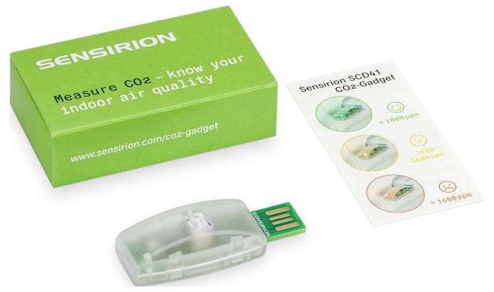 Zelená krabička s nápisem 'Měřte CO2 - poznejte kvalitu vašeho vnitřního vzduchu' s průhledným USB zařízením a kartou zobrazující úrovně CO2 se smajlíky.
