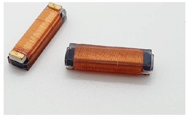 Dvě malé, obdélníkové oranžové cívky s měděným drátem, umístěné na bílém povrchu.