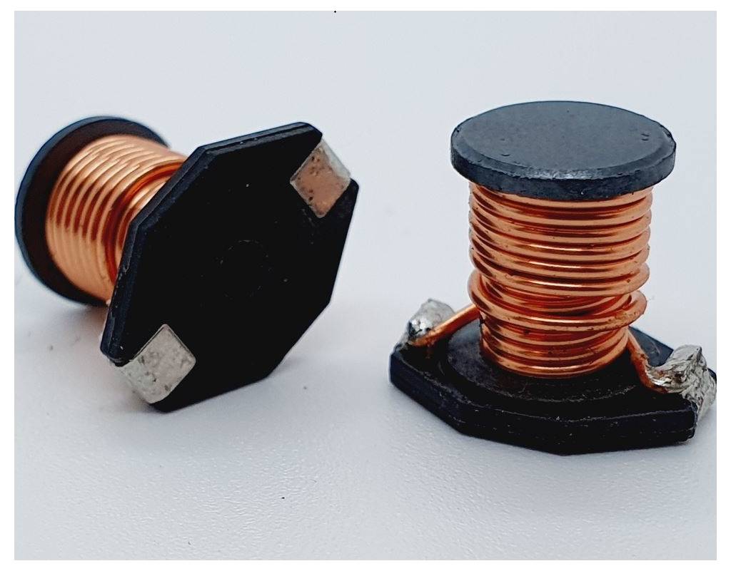 Dva válcové induktory s měděnými drátenými cívkami a černými základnami na bílém pozadí.