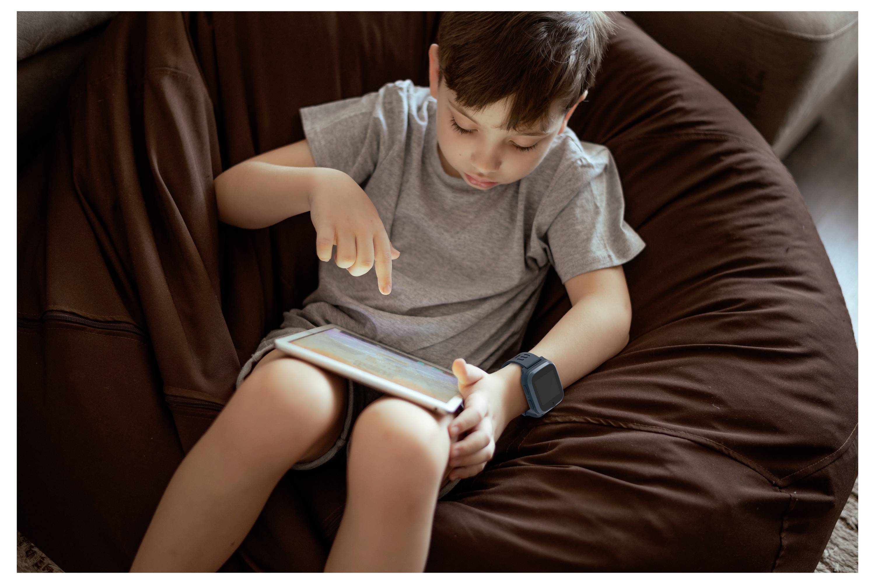 Dítě sedící na sedacím vaku, soustředěné na interakci s digitálním tabletem, ukazující prstem na obrazovku.