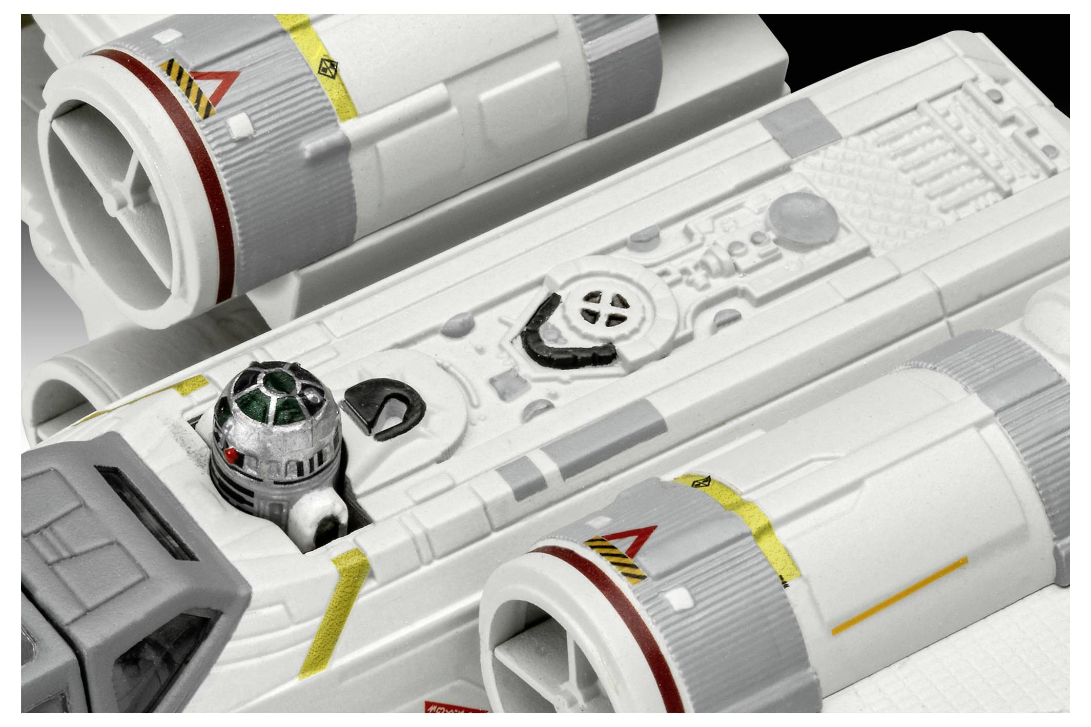 Malý droid sedí ve své schránce na futuristickém modelu kosmické lodi s detailními texturami a označeními, na černém pozadí.