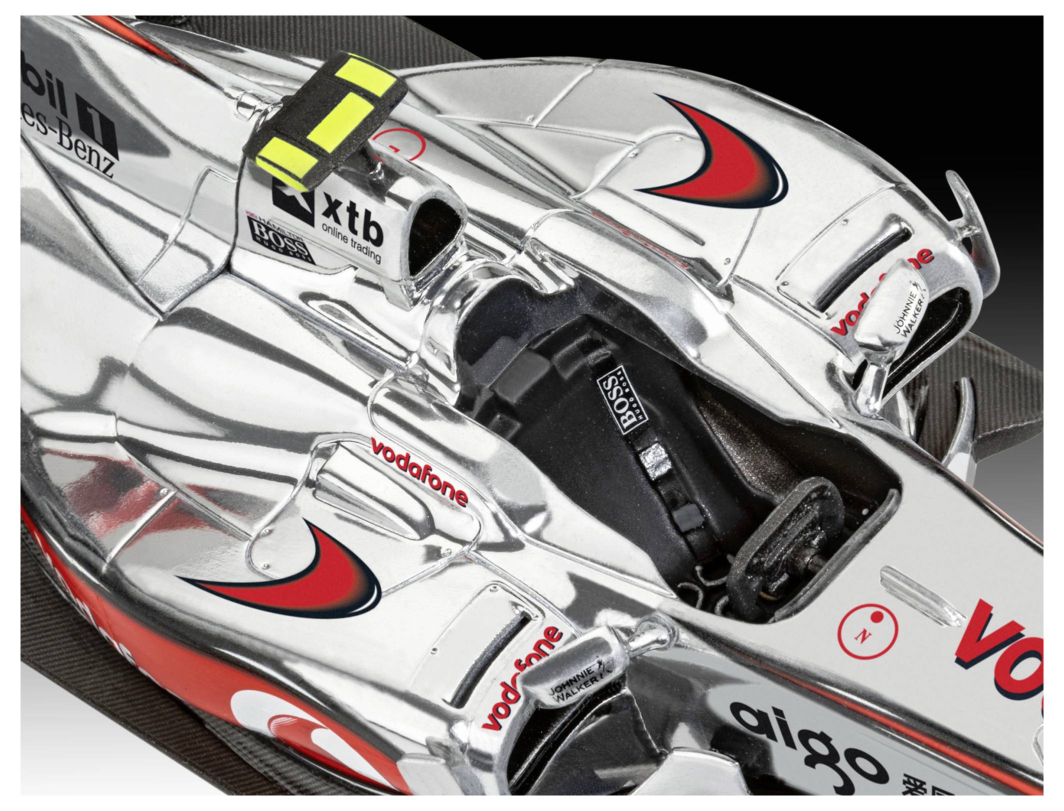 Detailní záběr z bezprostřední blízkosti na elegantní stříbrný kokpit závodního vozu Formule 1, který ukazuje reklamní loga a aerodynamické prvky.