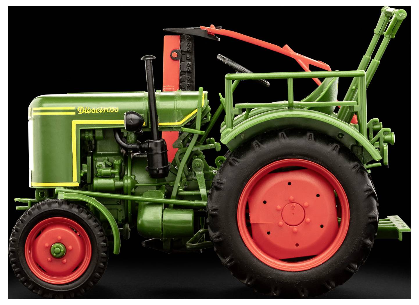 Vintage zelený a červený traktor na černém pozadí, prezentující jeho boční profil. Má charakteristická červená kola a detailní části motoru.