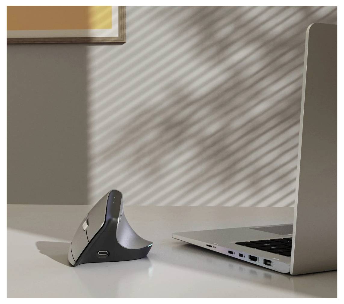 Elegantní bezdrátová vertikální počítačová myš na stole vedle stříbrného laptopů pod měkkým, filtrovaným světlem procházejícím žaluziemi.