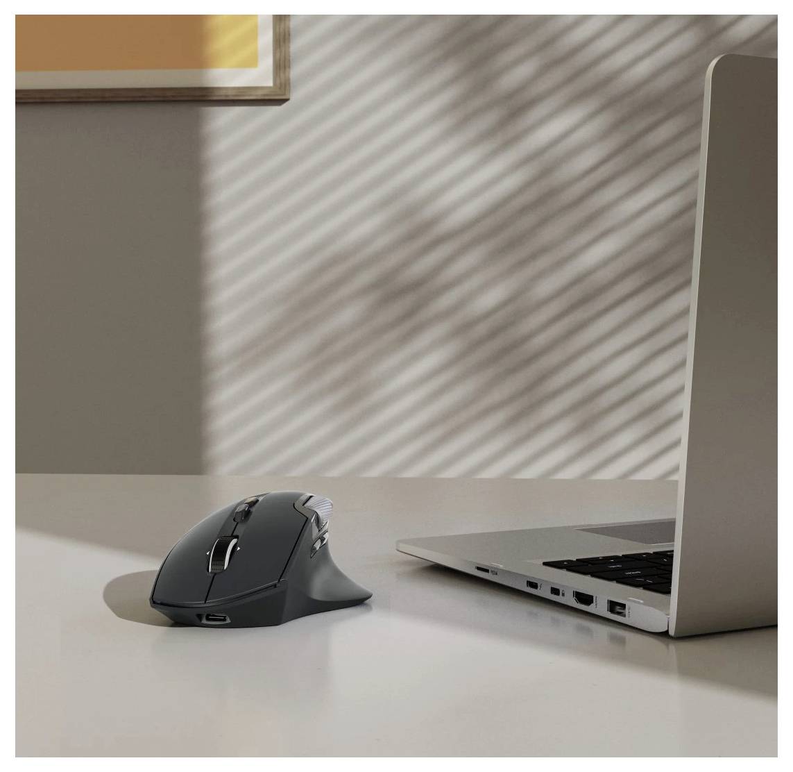 Bezdrátová myš vedle otevřeného laptopu na stole, přičemž sluneční světlo vytváří pruhované vzory na zdi a povrchu.