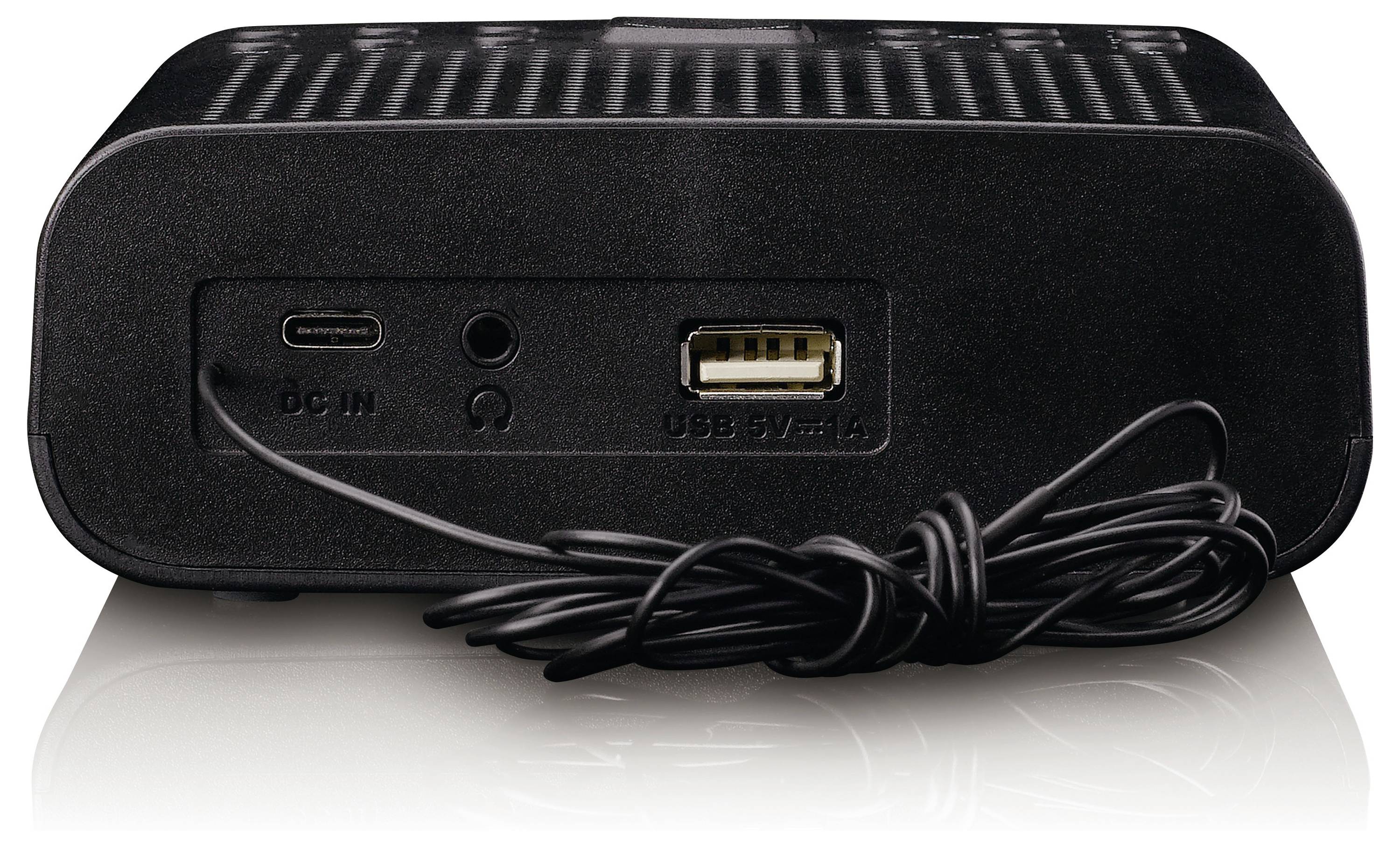 Černý elektronický přístroj s USB portem označeným „USB 5V 1A", DC vstupem a audio vstupem na zadní straně. Poblíž je svinutý černý kabel.