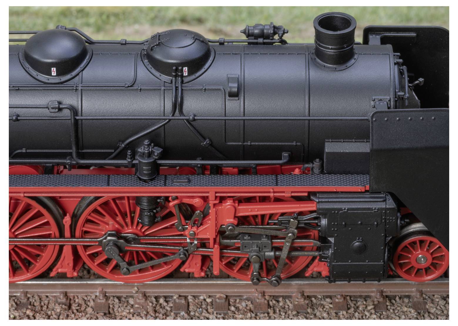 Detailní záběr boku vintage parní lokomotivy, který zvýrazňuje složité mechanické komponenty a výrazné červené a černé barvy.