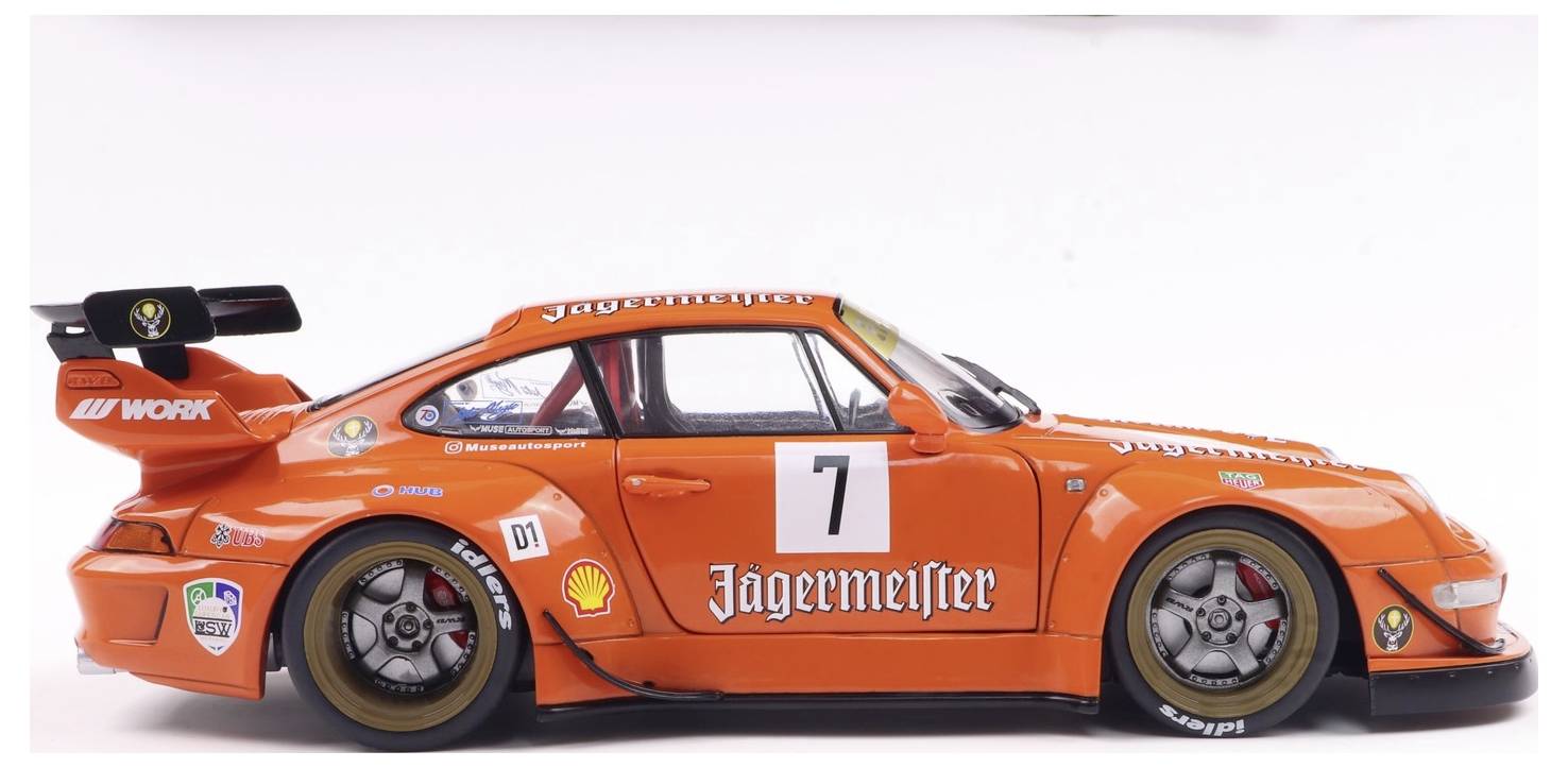 Oranžový závodní vůz s číslem 7 a reklamou Jägermeister na boku, s přídavným zadním křídlem a sponzorskými nálepkami.