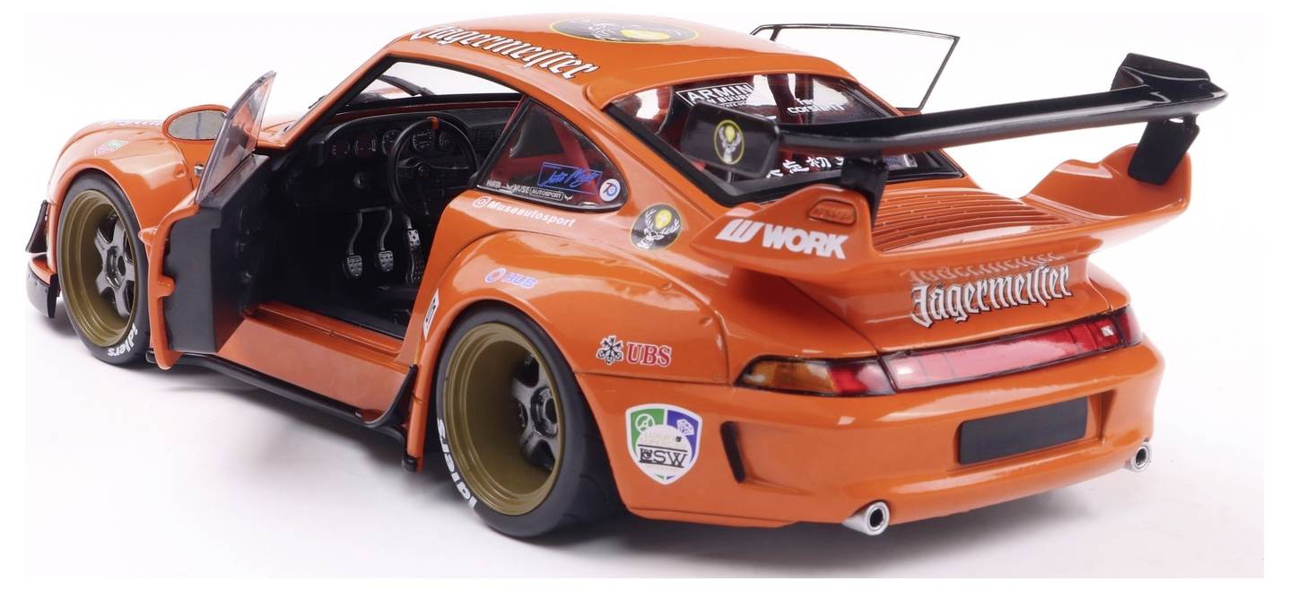 Oranžový vysoce výkonný sportovní vůz s широким bodykit, zadním křídlem a závodními samolepkami, s otevřenými dveřmi řidiče a detailně zobrazeným interiérem.