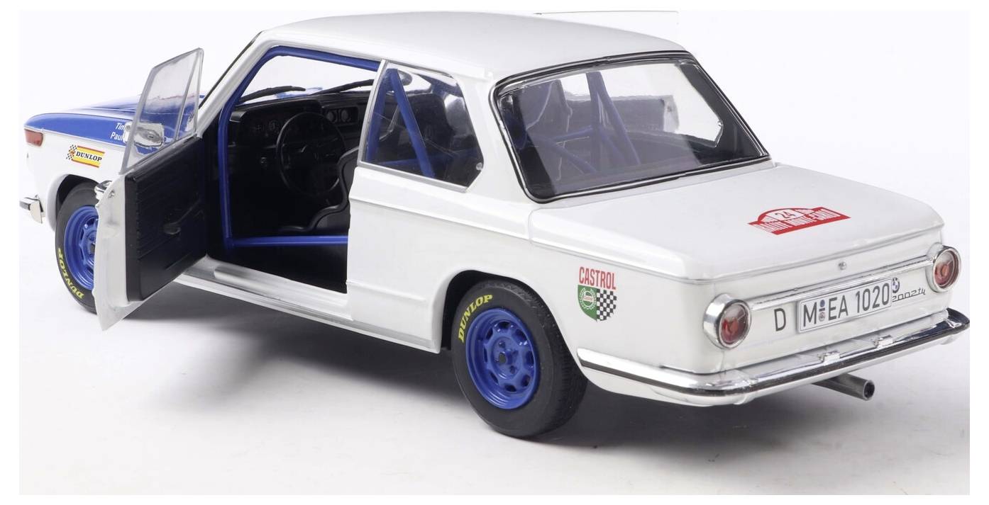 Bílý a modrý vintage model auta s otevřenými dveřmi, detailním interiérem a závodními samolepkami, pohled zezadu.