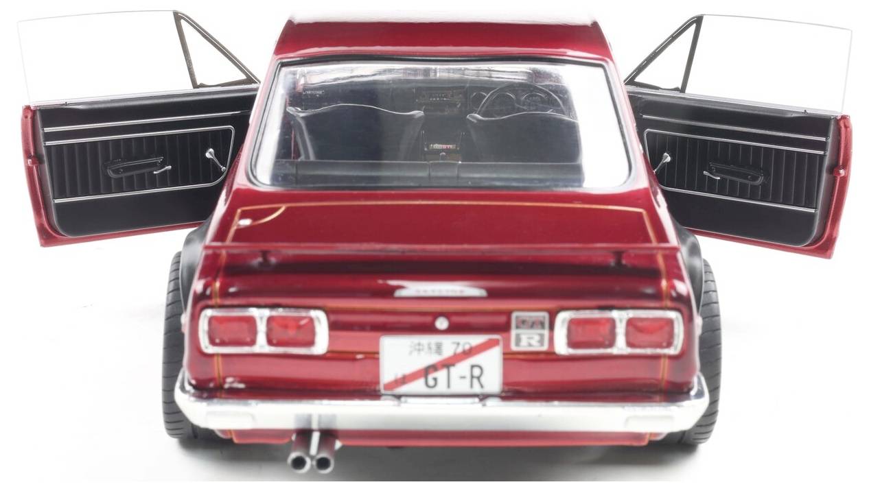 Červené vintage auto pohledené zezadu s otevřenými bočními dveřmi, které odhalují jeho interiér. Vyznačuje se klasickými designovými prvky a chromovými detaily.