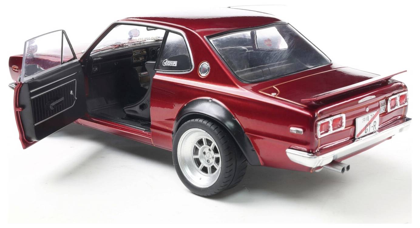 Model červeného vintage automobilu s otevřenými předními dveřmi řidiče, s detailně zobrazeným interiérem a chromovanými akcenty, zaparkovaný na bílém povrchu.