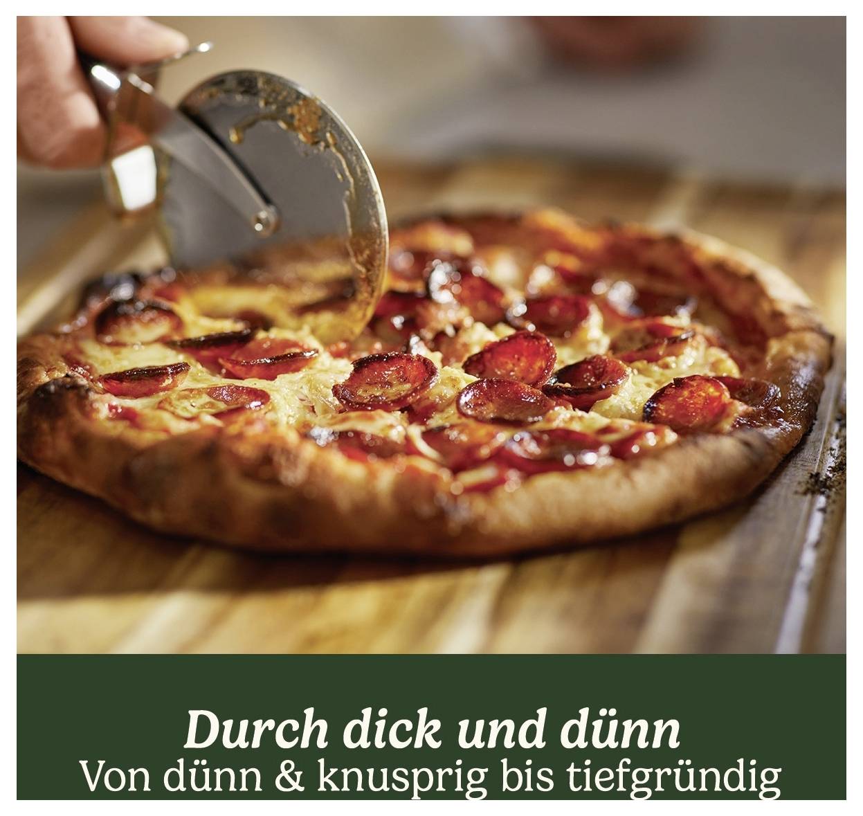 Čerstvá pizza je krájená pizzným nožem na dřevěné desce. Dole je umístěn slogan 'V dobrém i zlém'.