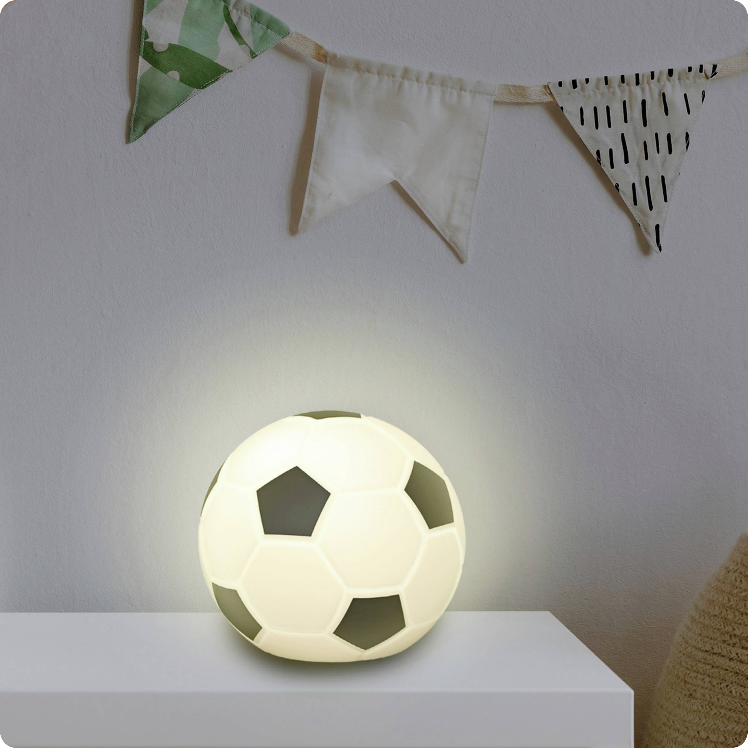 Zářící lampa ve tvaru fotbalového míče leží na bílém stole pod dekorativní vlajkovou girlandou.