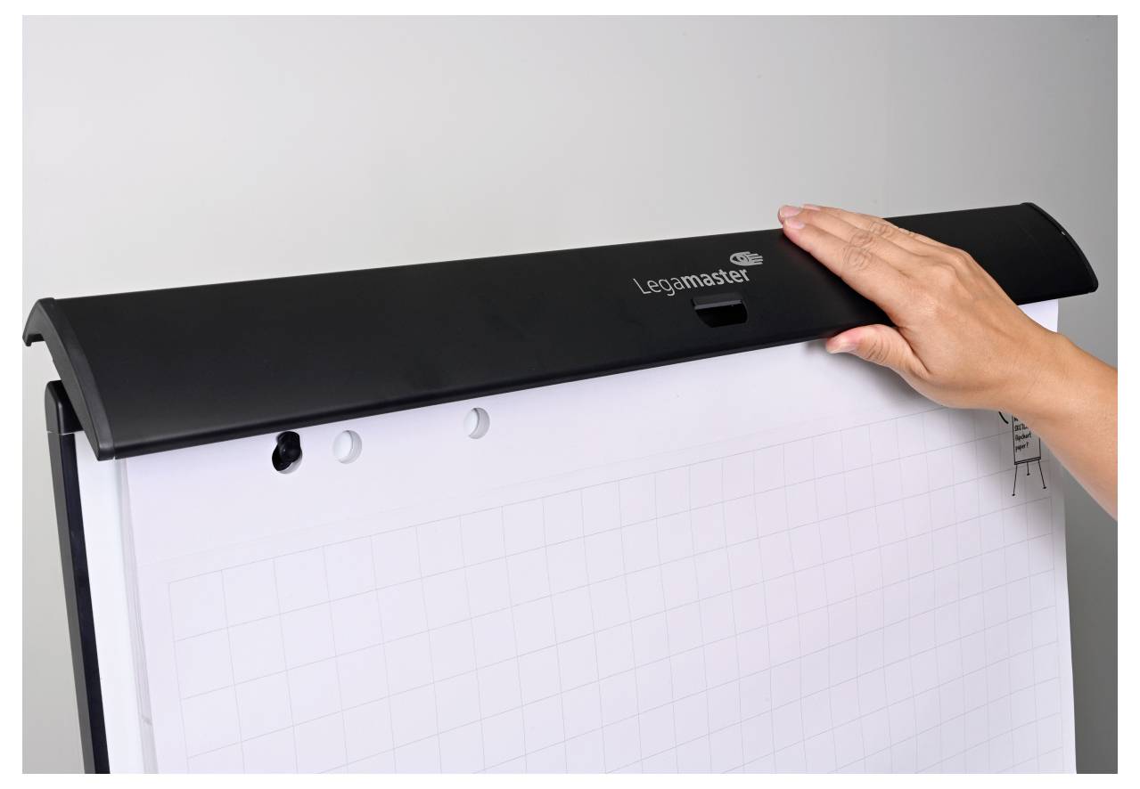 Ruka klade list milimetrového papíru na stojan na flip chart před světle šedým pozadím.