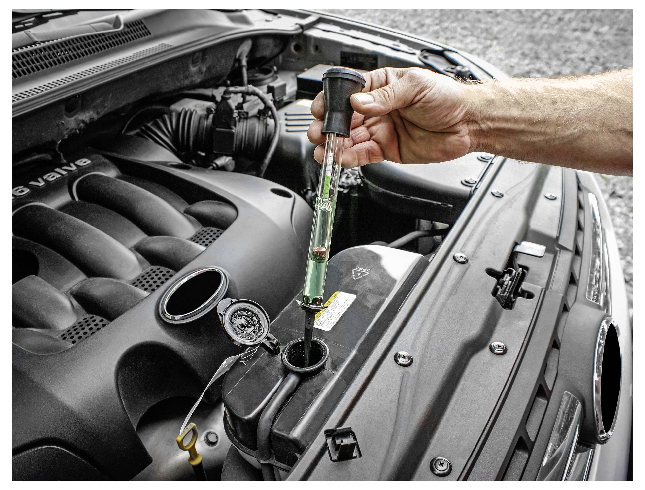 Osoba používá hustomer ke kontrole radiátorové kapaliny v automotoru, což ilustruje pravidelnou údržbu vozidla.