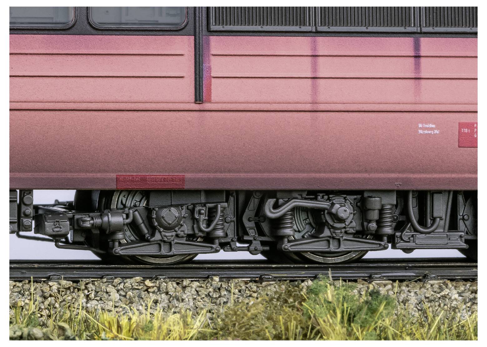 Detailní pohled na spodní část vlaku, který ukazuje kola, nápravy a část kolejnice, zvýrazňující jemné mechanické prvky a textury.