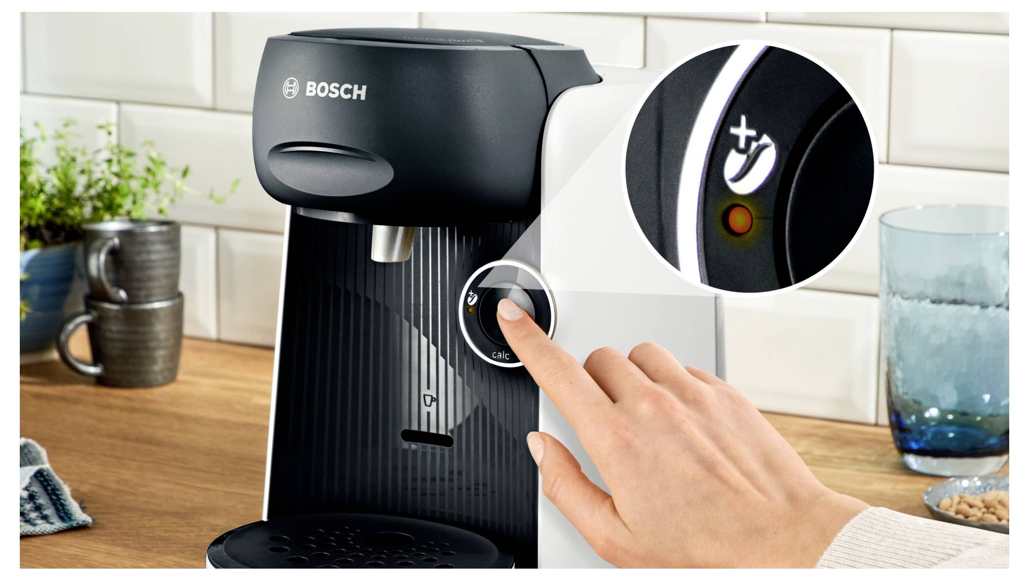 Ruka stiskává tlačítko na kávovaru značky Bosch, přičemž detail ikony napájení poukazuje na konkrétní funkci spotřebiče.