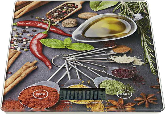 Digitální kuchyňská váha zobrazující '0,000 kg', obklopená kořením včetně chilli papriček, rozmarýnu a odměrnými lžičkami s mletými bylinkami.