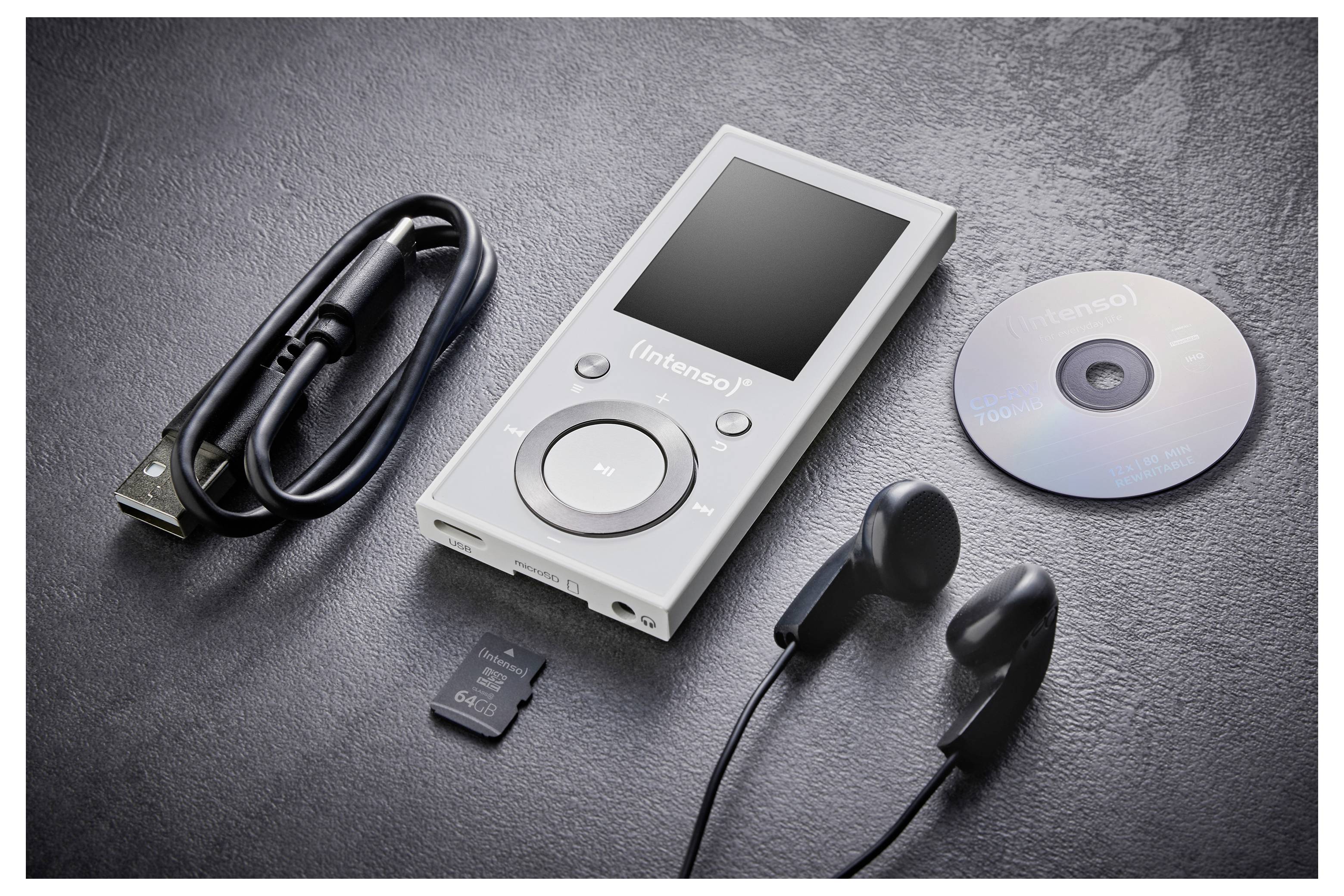 Šedý přenosný hudební přehrávač s sluchátky, USB kabelem, mini SD kartou a CD, vše umístěné na tmavém texturovaném povrchu.