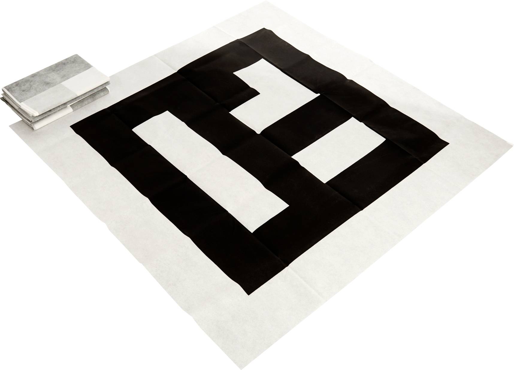 Velká textilní umělecká práce zobrazuje odvážný geometrický vzor z černých a bílých čtverců na bílém pozadí, vedle níž je složená vrstva podobných textilií.