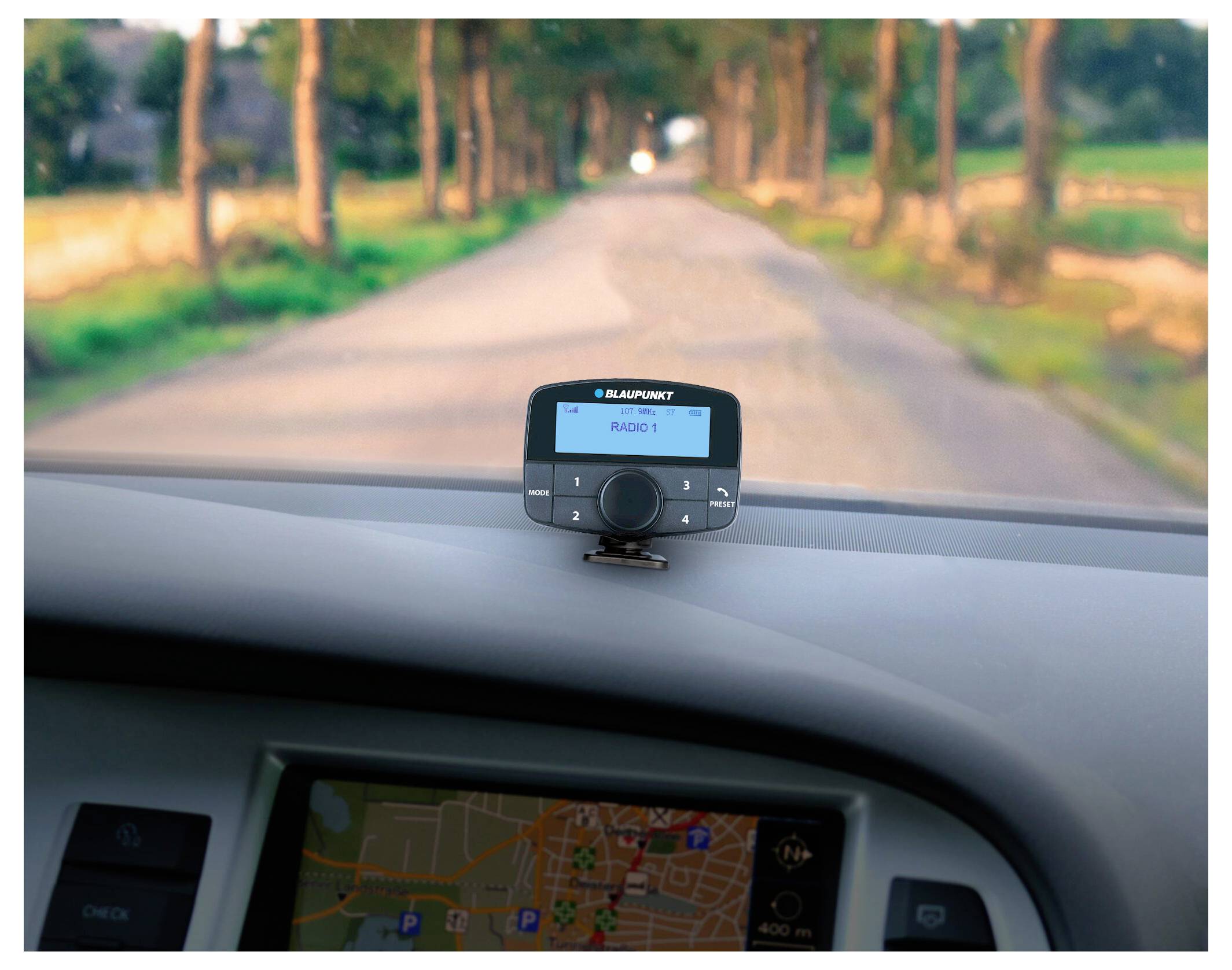 Na automobilovém přístrojovém panelu se zobrazuje navigační systém s mapou venkovské silnice. Rádio Blaupunkt zobrazuje "Radio 1" v jasném prostředí.