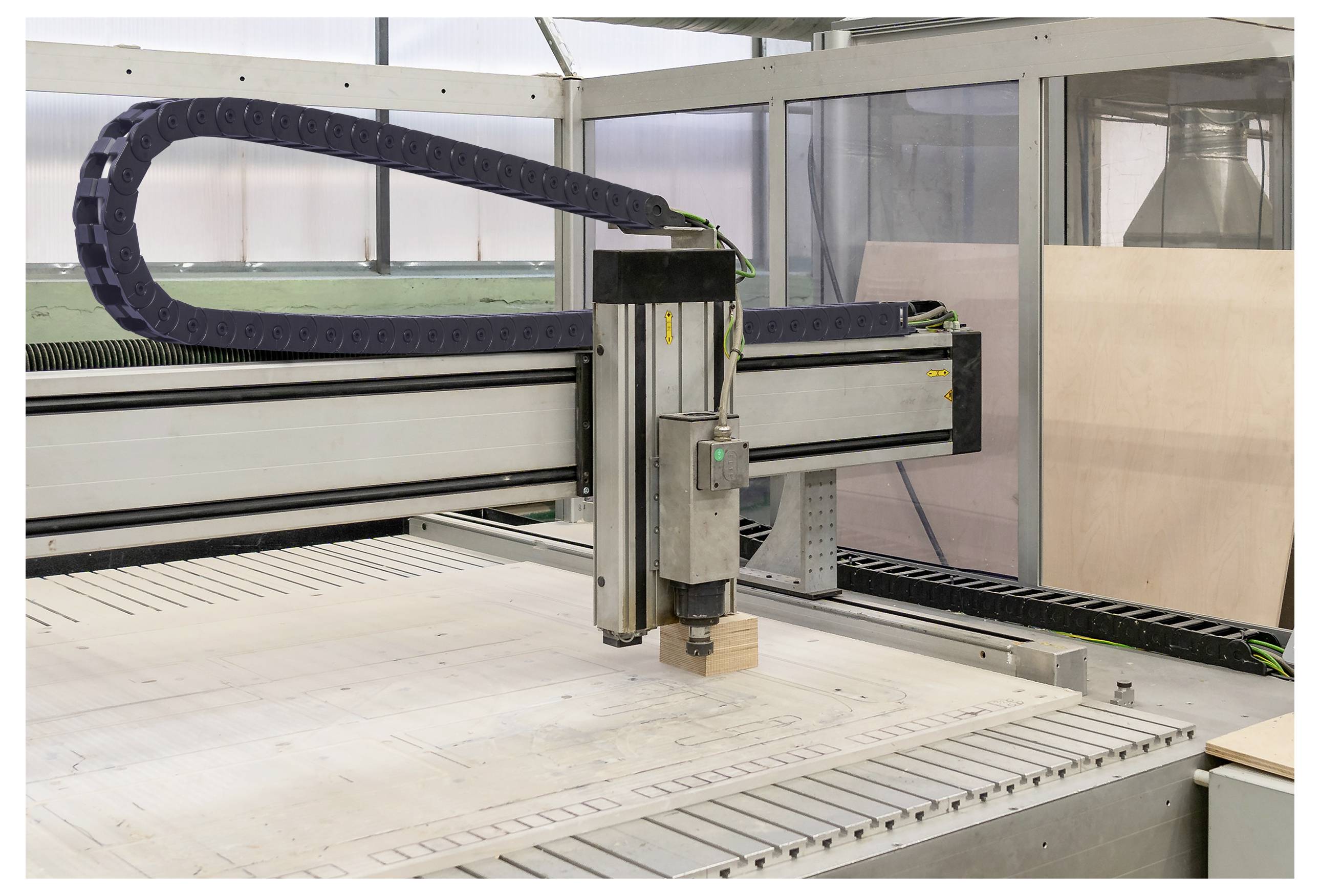 CNC stroj vyřezávající design do dřevěné desky s viditelným kovovým rámem a ochranným krytem v pozadí.