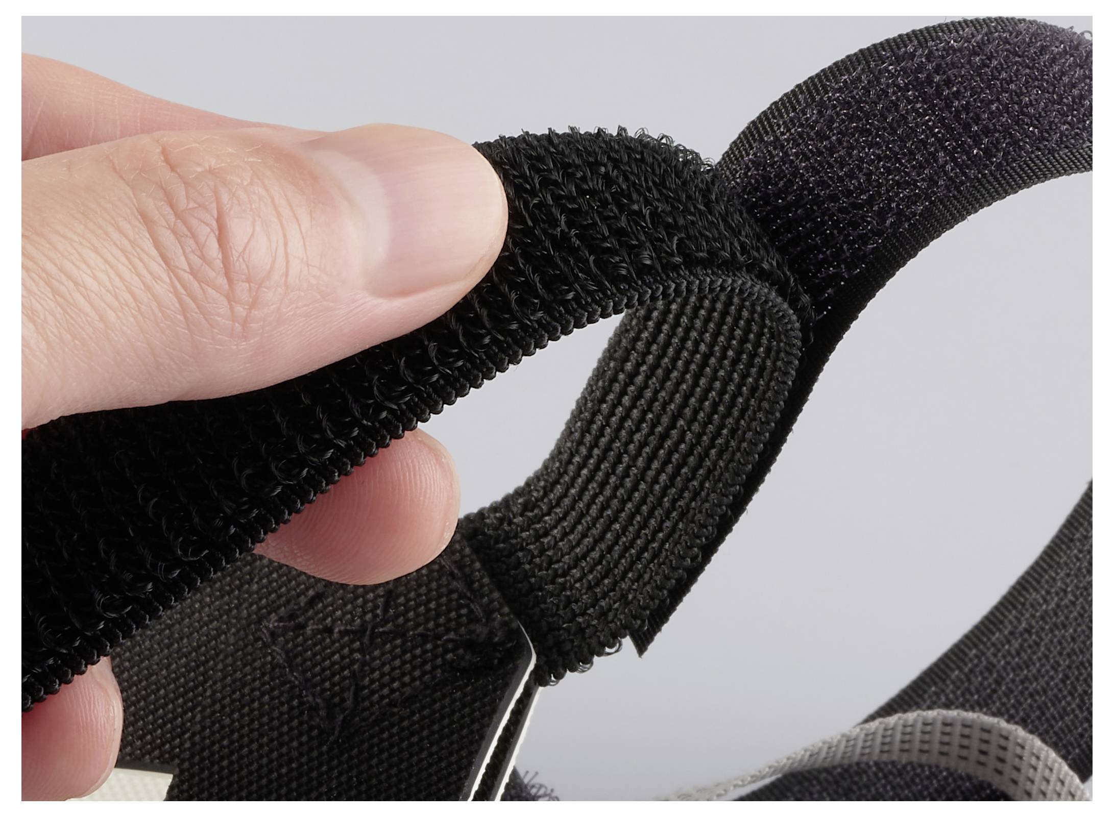 Detailní záběr na ruku, která upravuje suchý zip látkového předmětu, demonstrujícího, jak jej zapnout nebo rozepnout pro bezpečné uzavření.