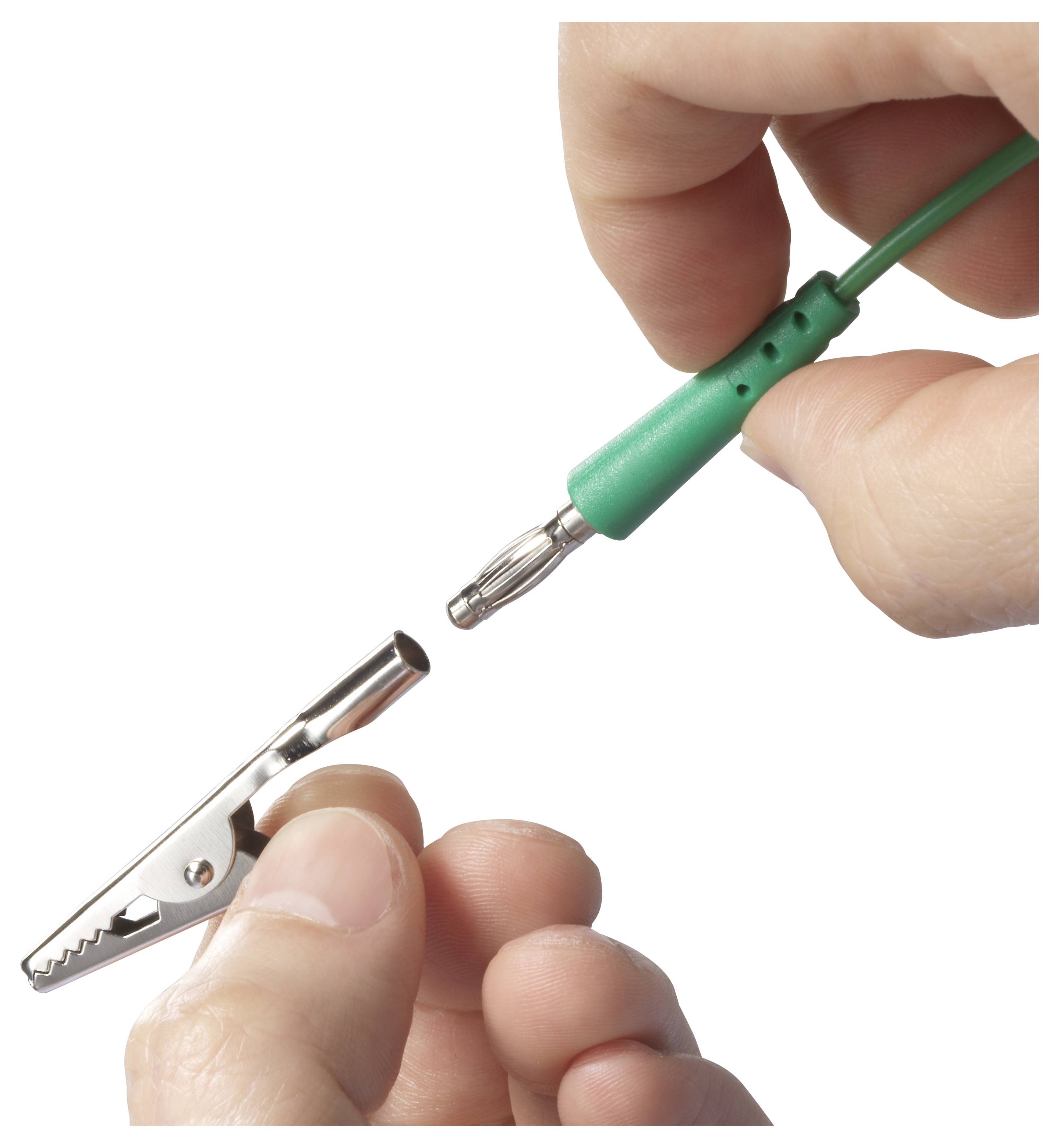 Osoba připojí zelený kabel s kovový zásuvkou na krokodýlí sponu drženou druhou rukou.