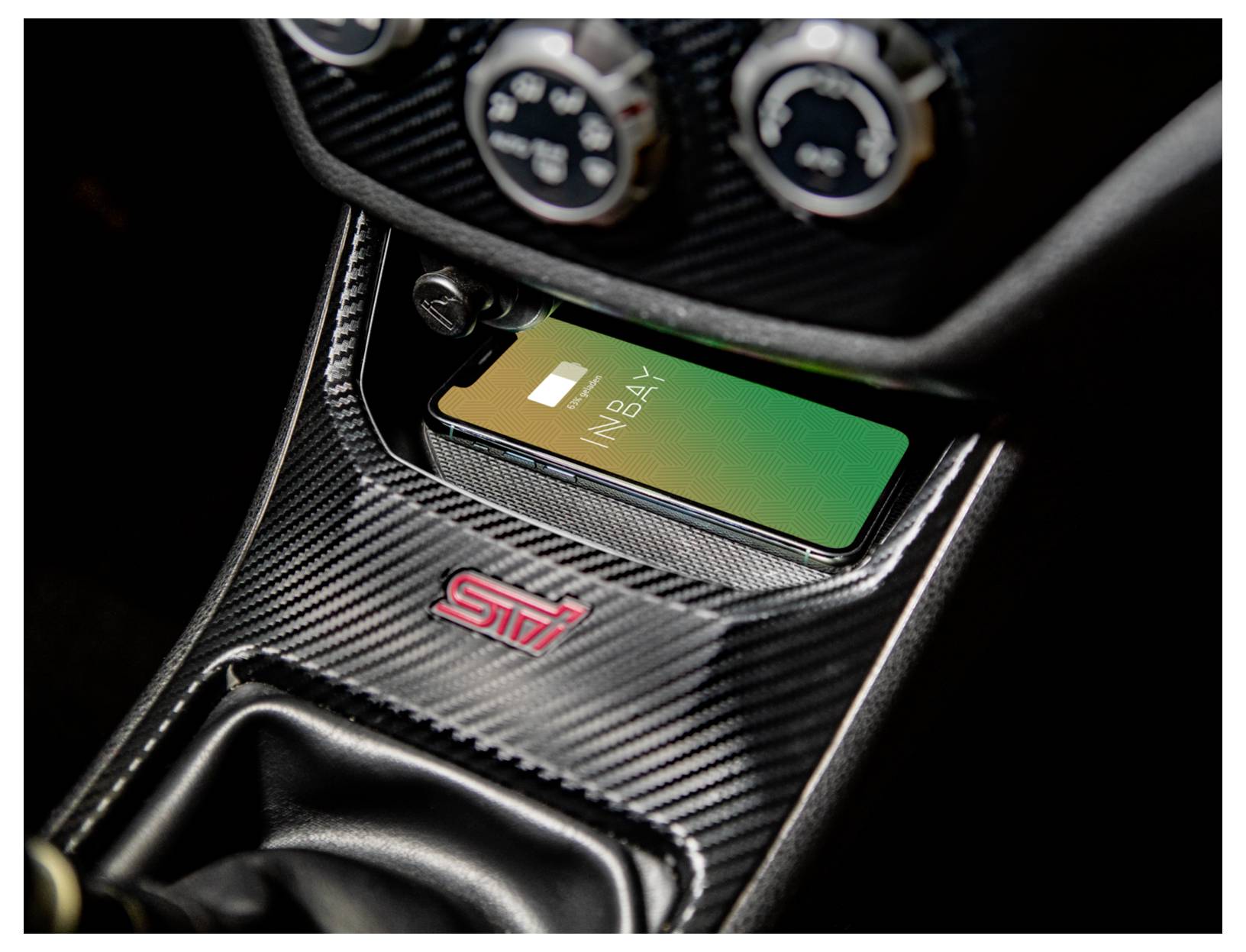 Chytrý telefon nabíjený bezdrátově v konzoli automobilu Subaru STI s dekorací z uhlíkového vlákna a logem STI.