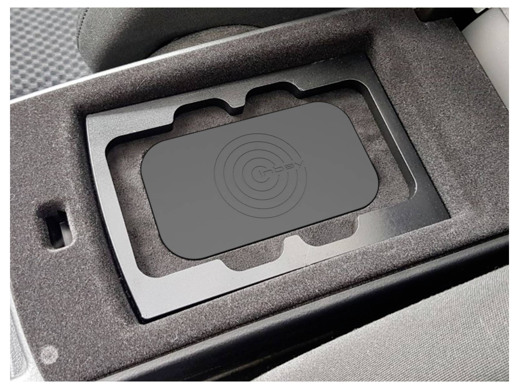 Černá bezdrátová nabíjecí podložka zapuštěná v pěnové vložce automobilového středového panelu, s cílovou ikonou na nabíjecí ploše.