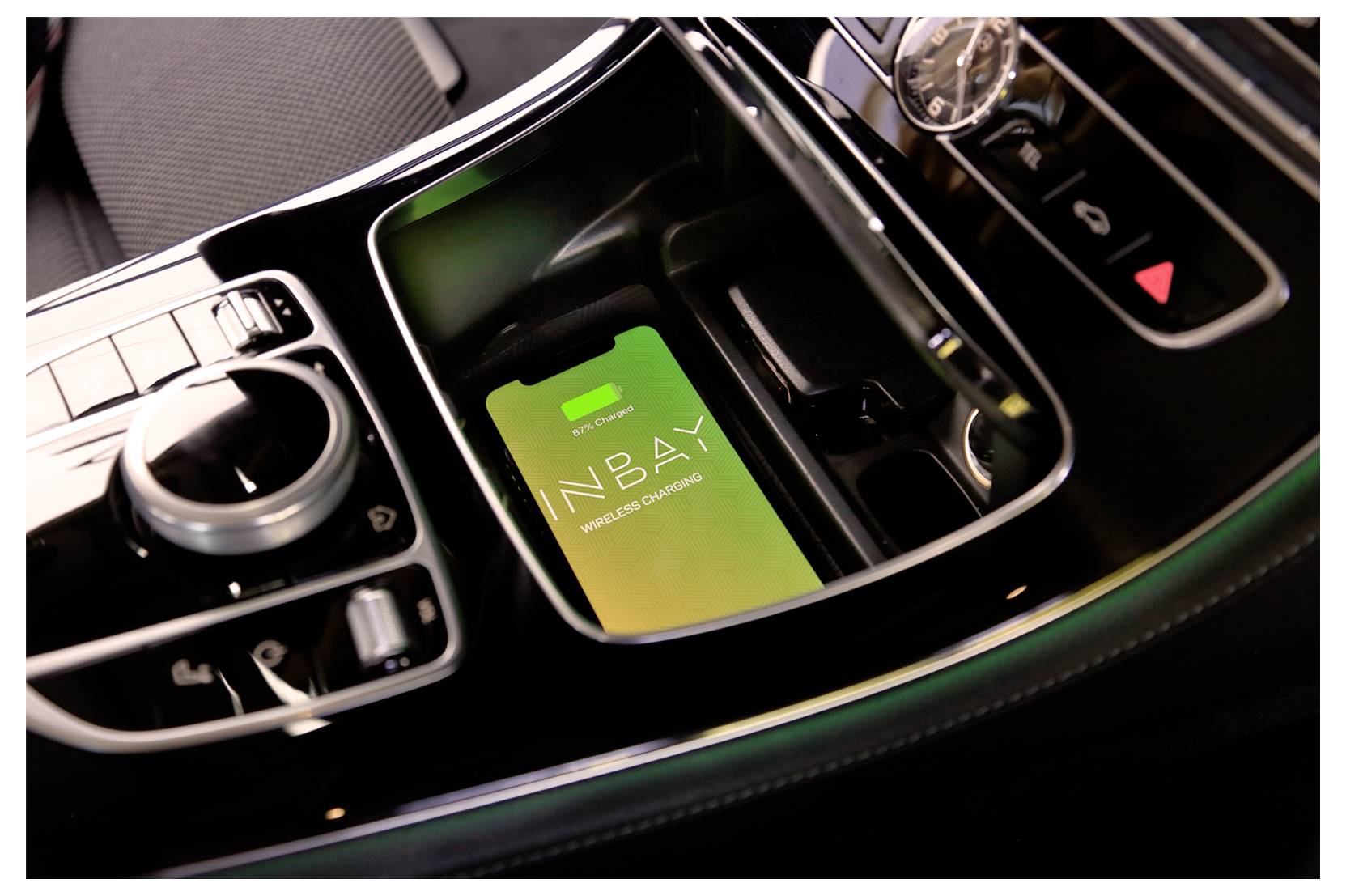 Středová konzola automobilu se smartphonem zobrazujícím 'INBABY', umístěným v bezdrátovém nabíjecím prostoru vedle tlačítek klimatizace a ovládání.