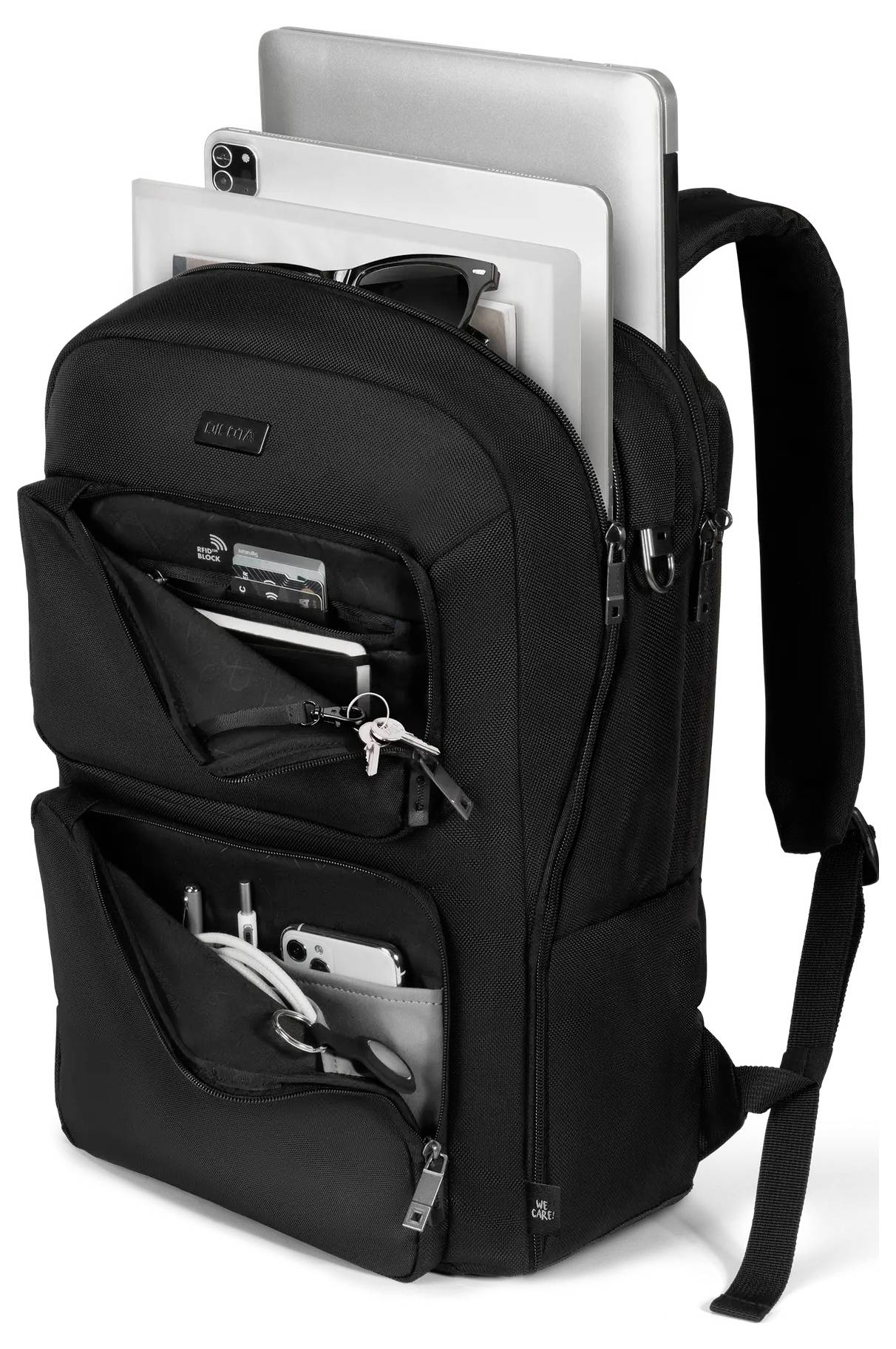 Černý batoh s více přihrádkami obsahující laptop, tablet, sluneční brýle, časopis, klíče a různé drobné věci.