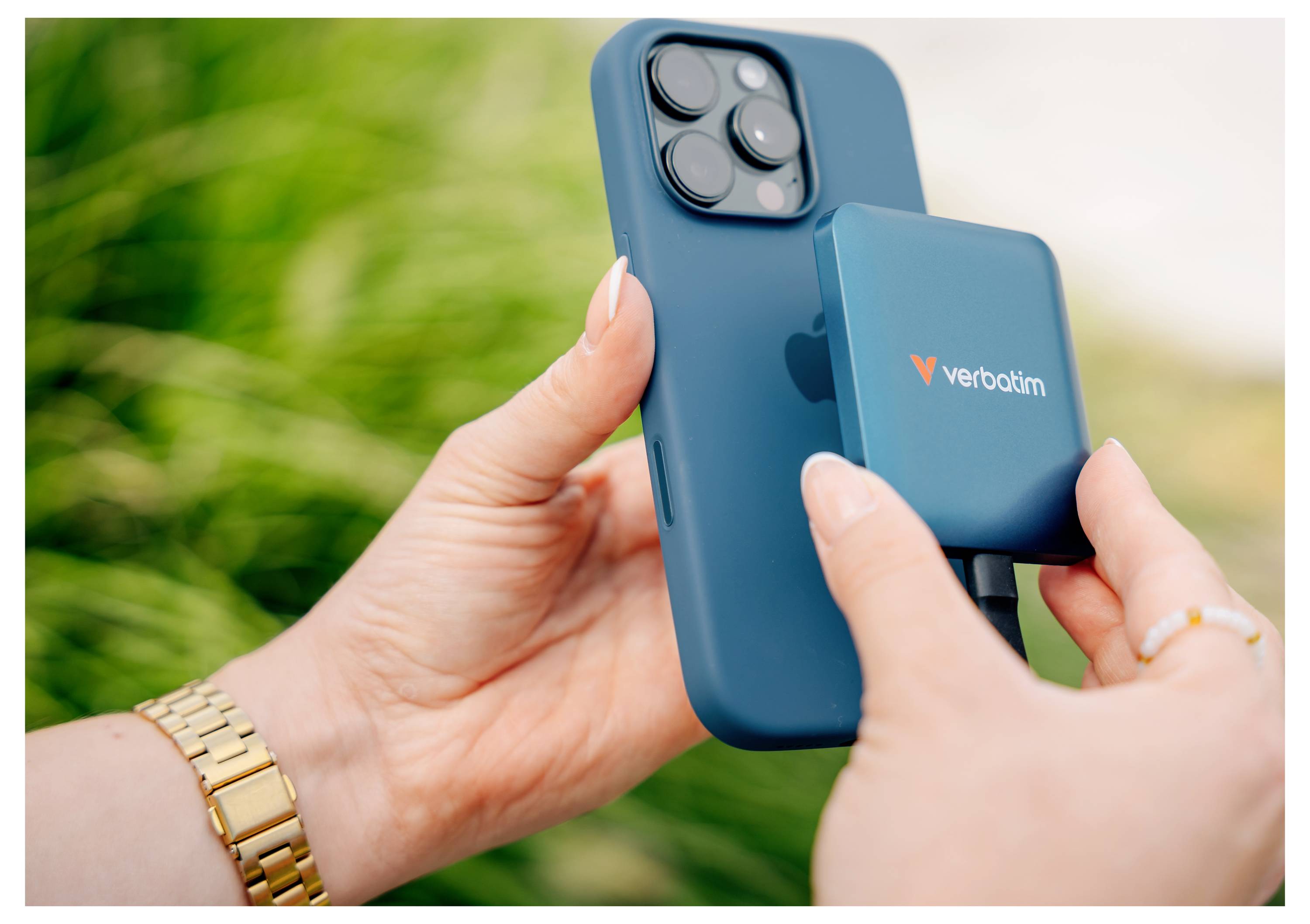 Ruce připevňují modrou magnetickou powerbanku Verbatim na zadní stranu modrého iPhonu venku.