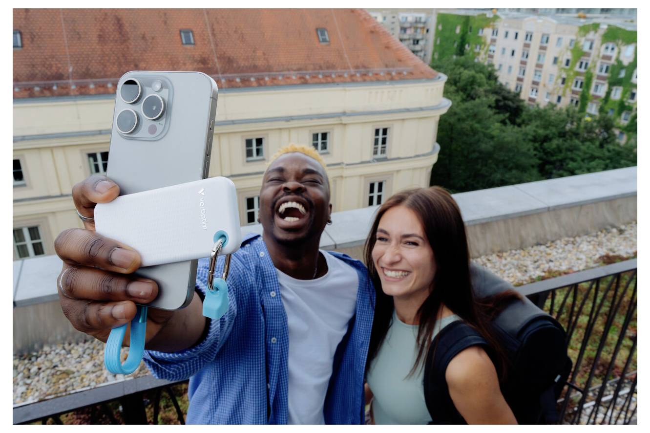 Dva usmívající se přátelé si pořizují selfie na střeše chytrým telefonem s městskými budovami v pozadí.